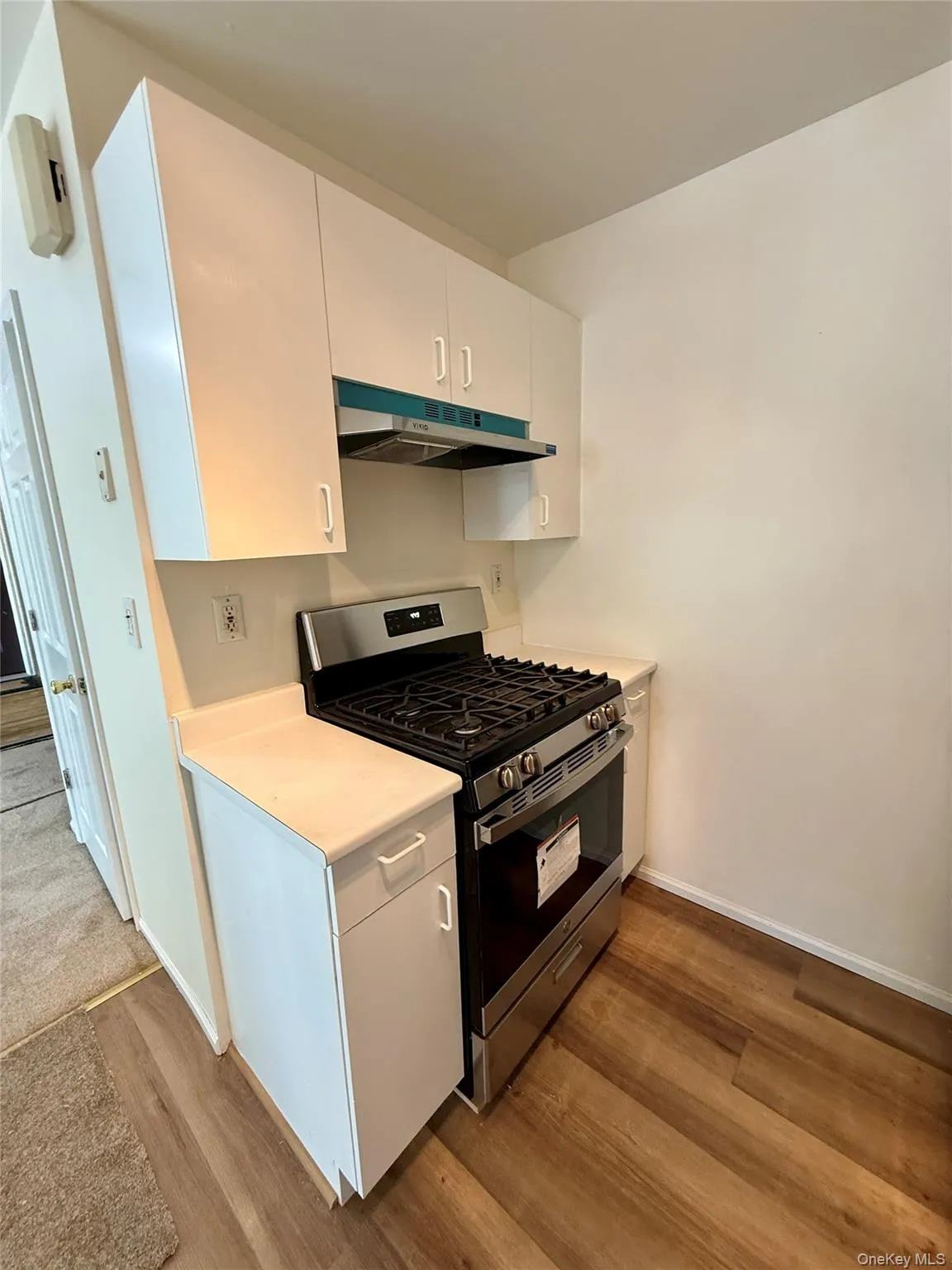 White cabinetry with sleek hardware, stainless steel range with gas cooktop, light-toned countertops, and wood-finish flooring White cabinetry with sleek hardware, stainless steel range with gas cooktop, light-toned countertops, and wood-finish flooring
