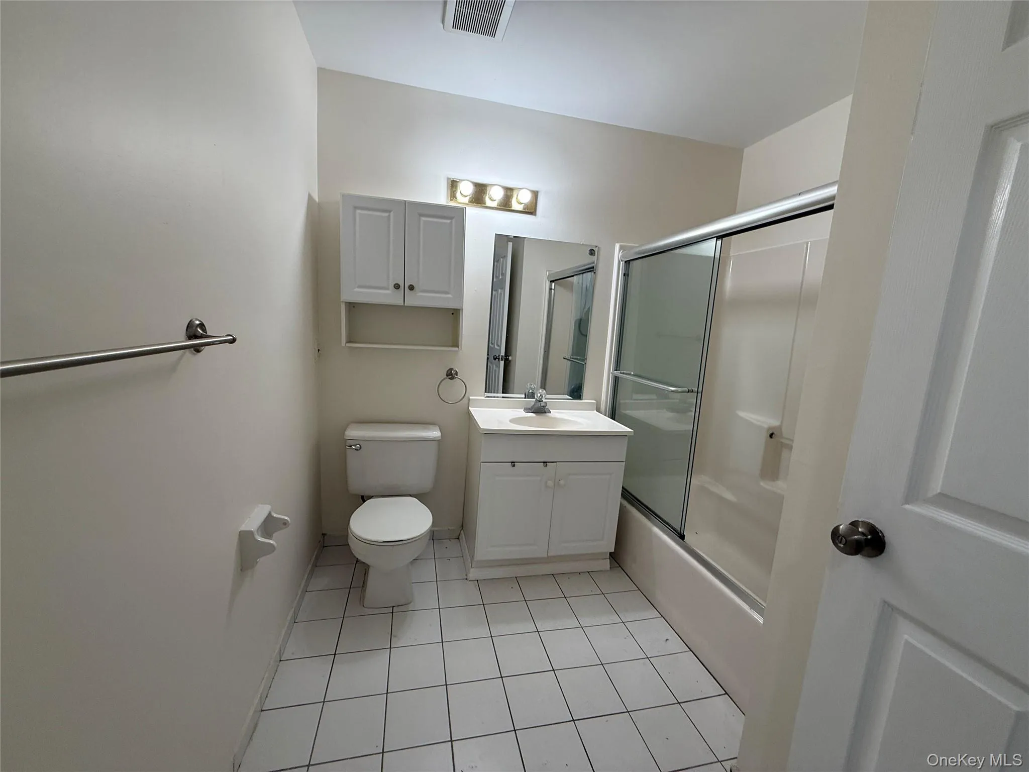 White tile flooring, single vanity with integrated sink, chrome faucet, mirrored medicine cabinet, and glass-enclosed shower White tile flooring, single vanity with integrated sink, chrome faucet, mirrored medicine cabinet, and glass-enclosed shower