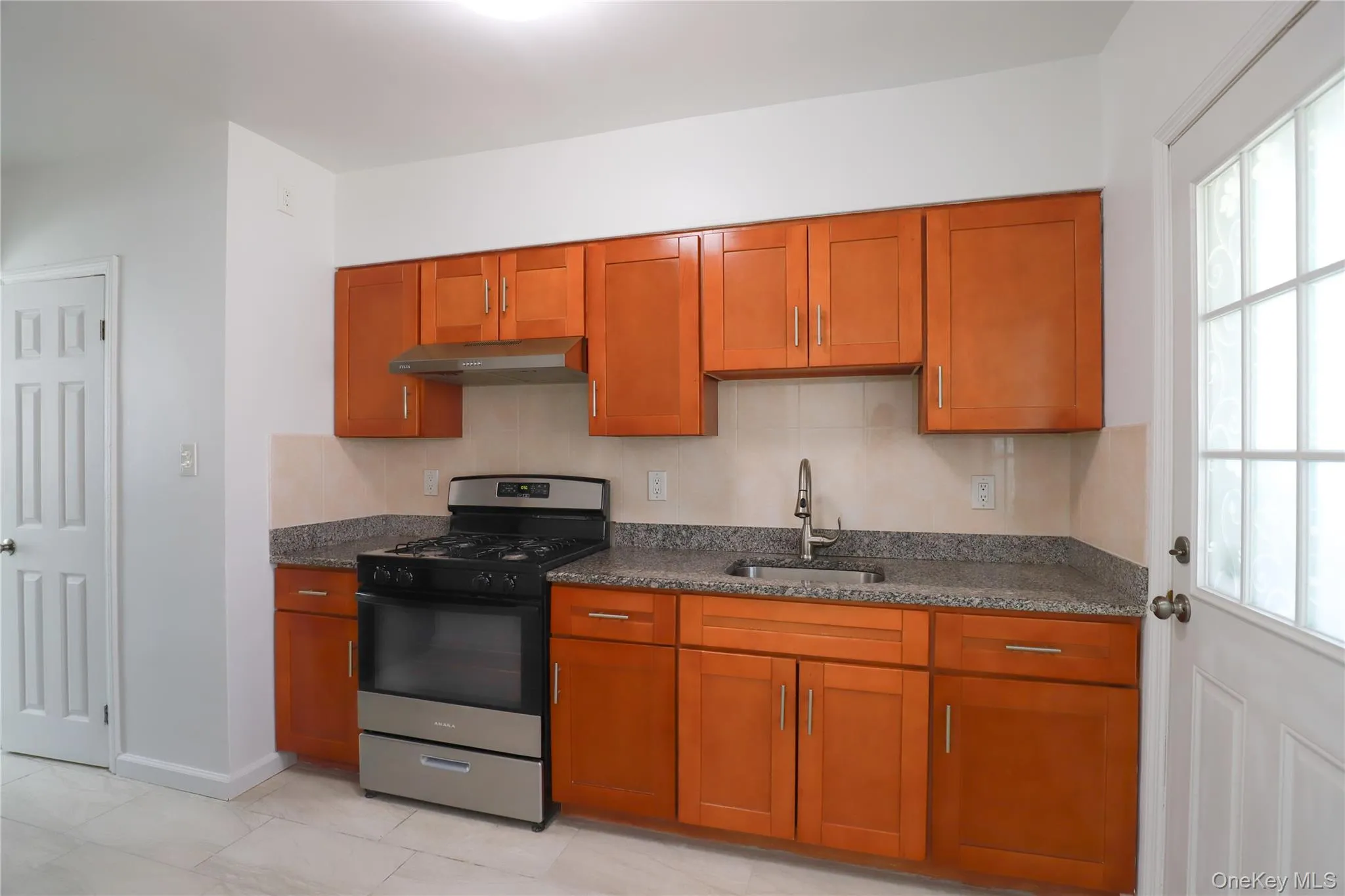 Kitchen featuring wood-finish cabinetry, stainless steel appliances, granite-style countertops, and a tile backsplash Kitchen featuring wood-finish cabinetry, stainless steel appliances, granite-style countertops, and a tile backsplash