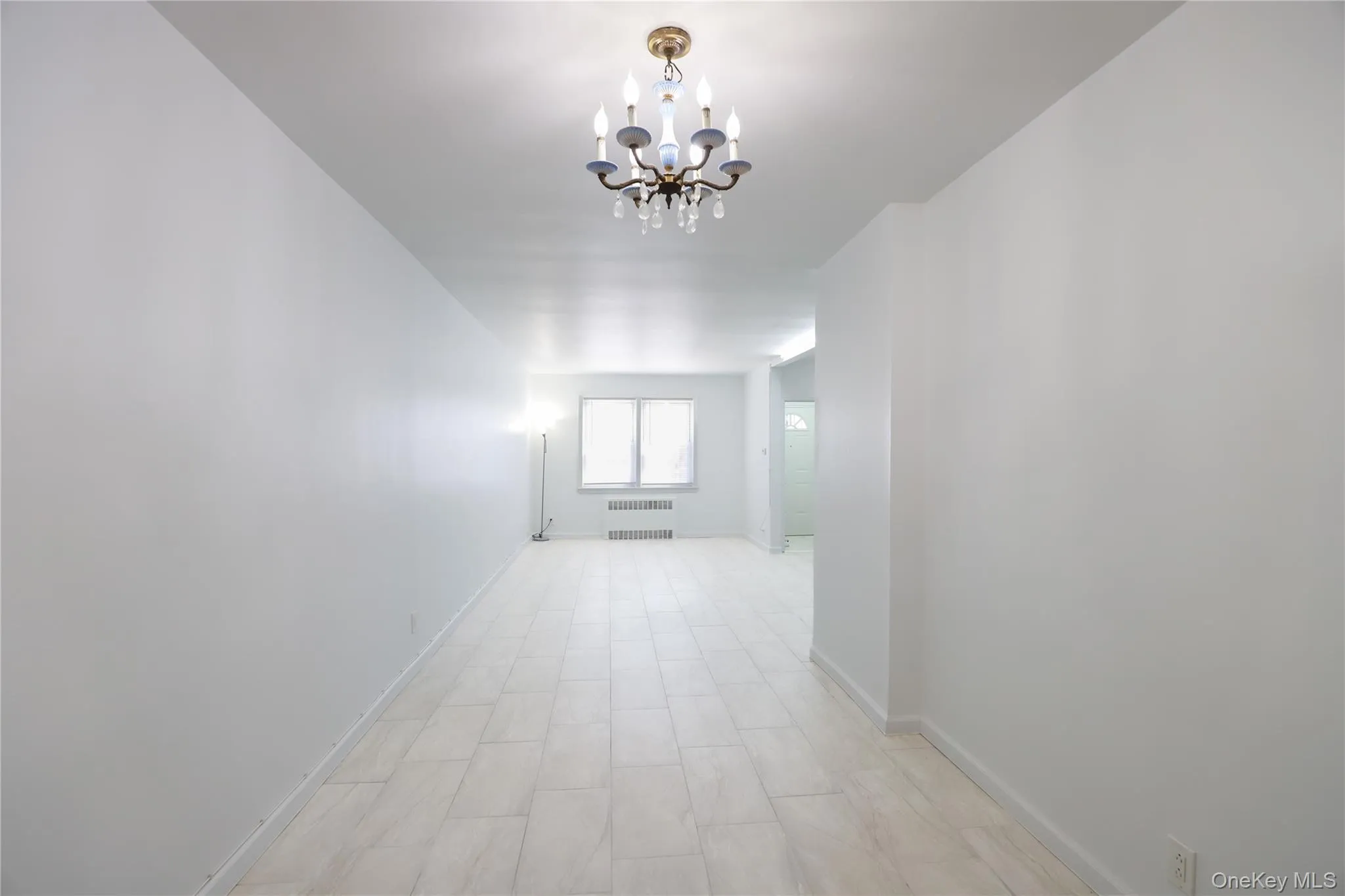 Expansive living room featuring light-toned flooring, a classic chandelier, and crisp white walls Expansive living room featuring light-toned flooring, a classic chandelier, and crisp white walls