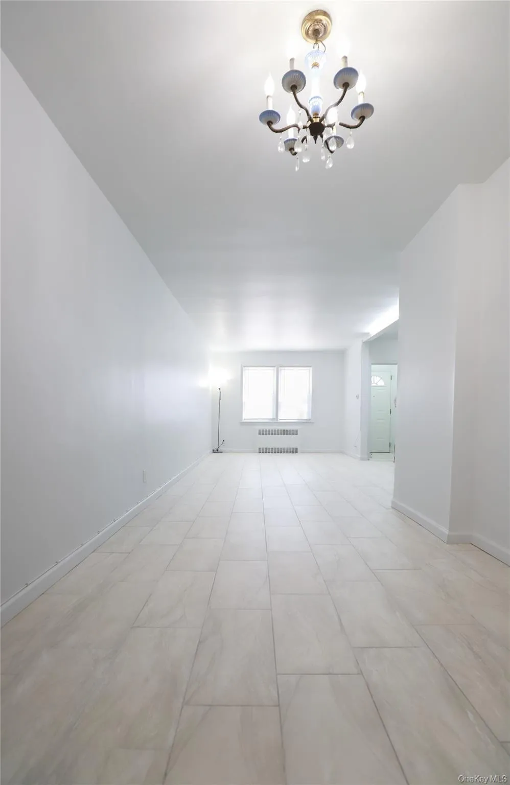 Expansive living room featuring light-toned flooring, a classic chandelier, and crisp white walls Expansive living room featuring light-toned flooring, a classic chandelier, and crisp white walls