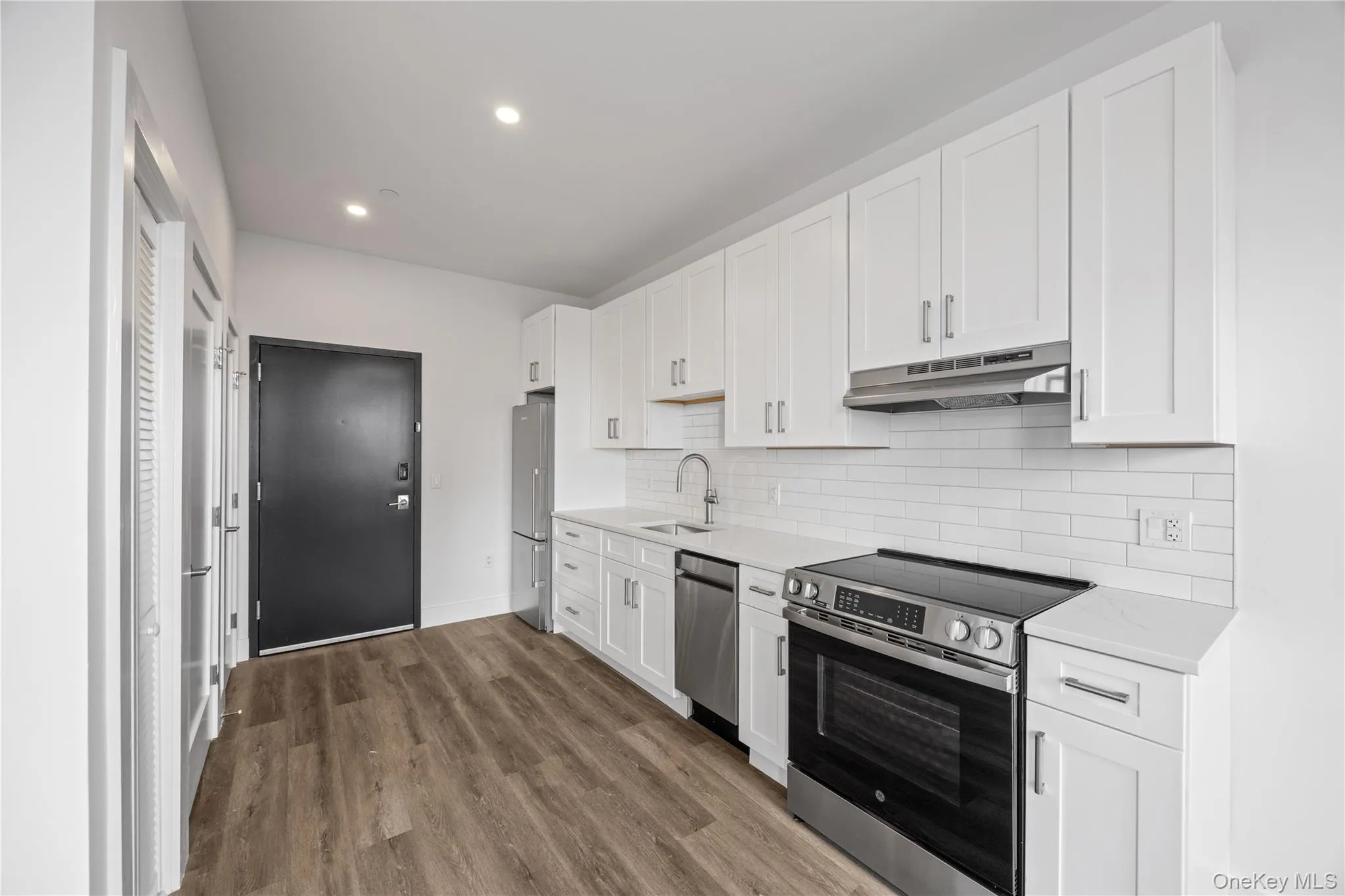 Modern kitchen with white shaker cabinetry, stainless steel appliances, white subway tile backsplash, and wood-finish flooring Modern kitchen with white shaker cabinetry, stainless steel appliances, white subway tile backsplash, and wood-finish flooring