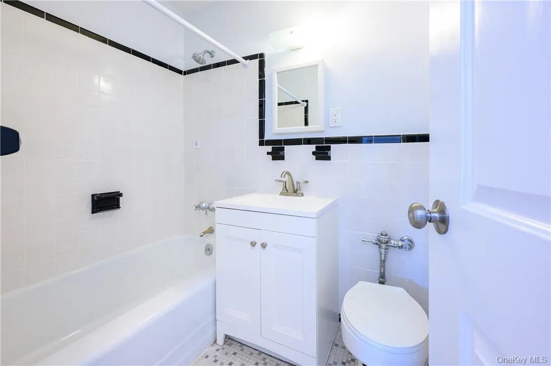 Full bathroom featuring toilet, tile patterned floors, tiled shower / bath, vanity, and tile walls Full bathroom featuring toilet, tile patterned floors, tiled shower / bath, vanity, and tile walls