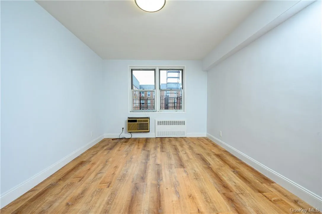 Empty room with a wall mounted AC, radiator, and light hardwood / wood-style floors Empty room with a wall mounted AC, radiator, and light hardwood / wood-style floors