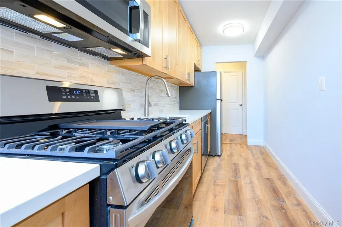 Kitchen with backsplash, stainless steel appliances, sink, and light wood-type flooring Kitchen with backsplash, stainless steel appliances, sink, and light wood-type flooring