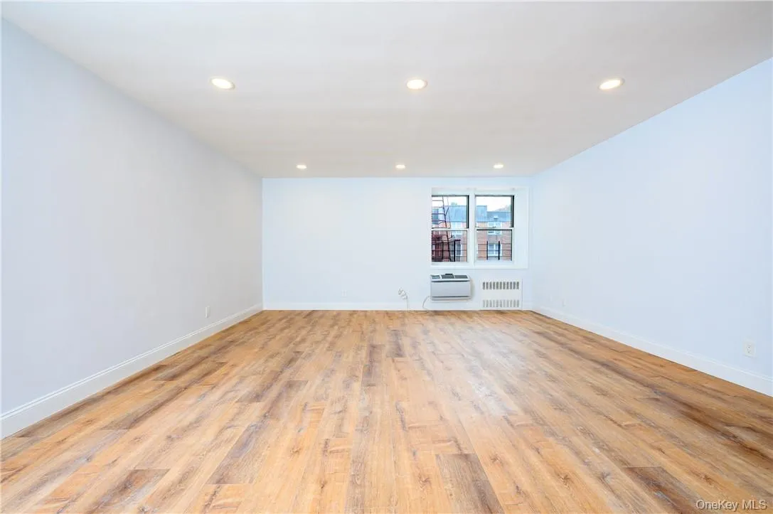Unfurnished room with a wall mounted AC, radiator, and light wood-type flooring Unfurnished room with a wall mounted AC, radiator, and light wood-type flooring