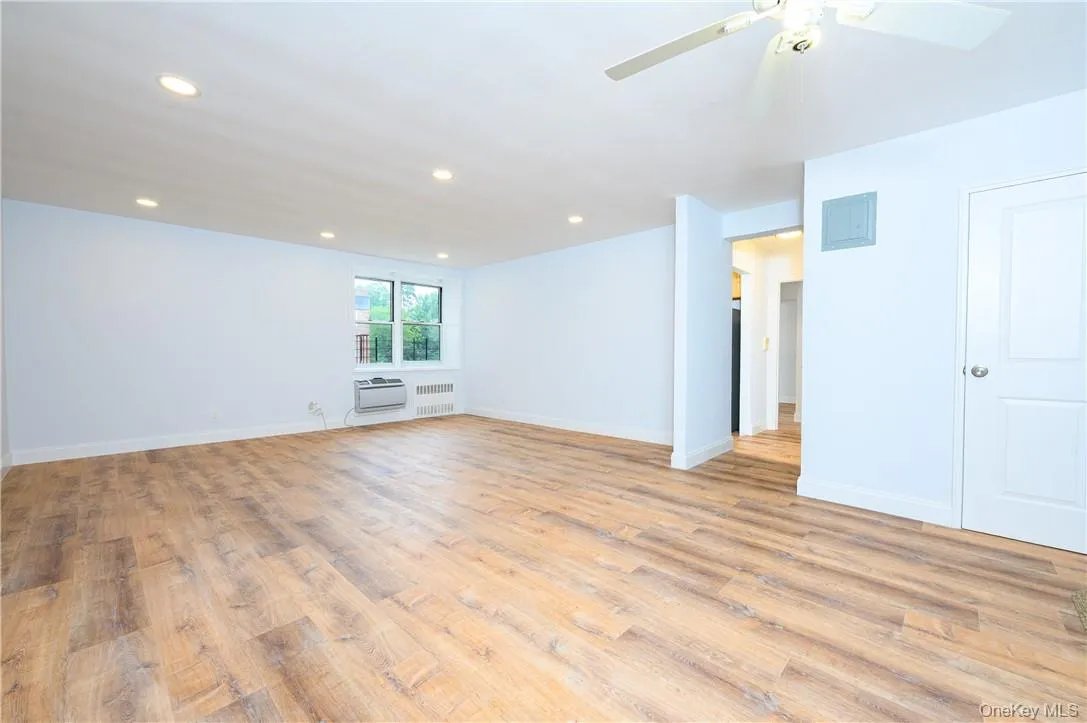 Spare room featuring light wood-type flooring, ceiling fan, radiator, and a wall mounted air conditioner Spare room featuring light wood-type flooring, ceiling fan, radiator, and a wall mounted air conditioner