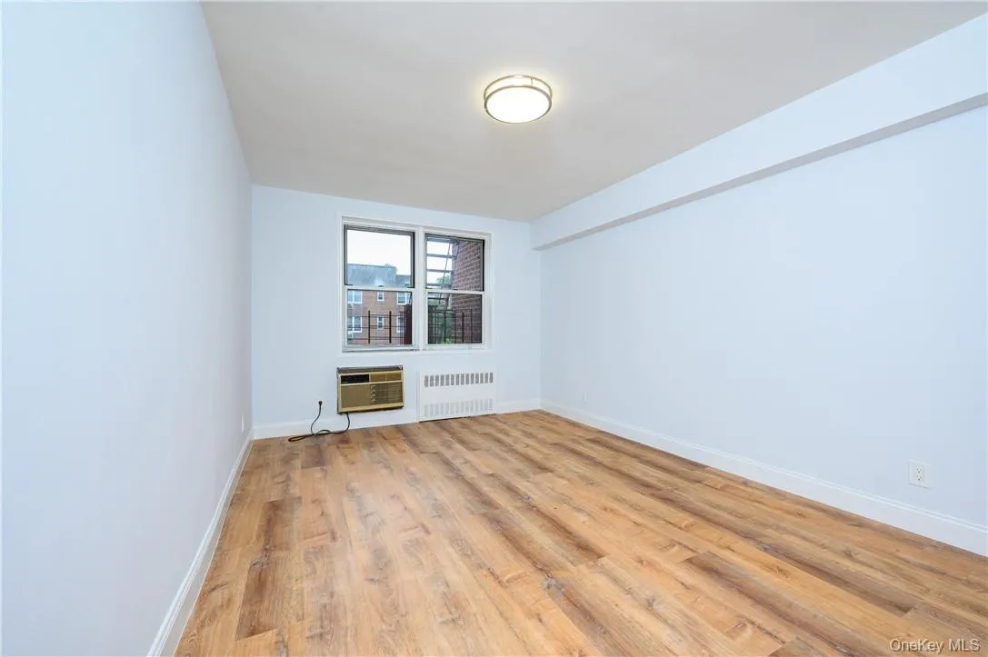Unfurnished room featuring a wall mounted AC, radiator, and wood-type flooring Unfurnished room featuring a wall mounted AC, radiator, and wood-type flooring