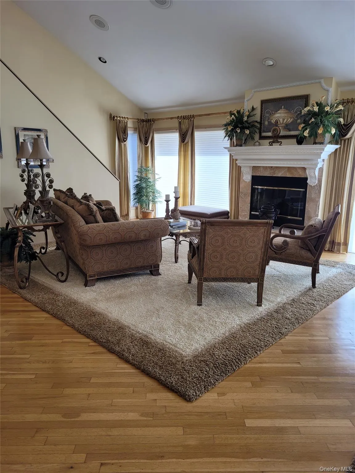 Wood-finish flooring, recessed lighting, and a fireplace with a stone surround and ornate mantel Wood-finish flooring, recessed lighting, and a fireplace with a stone surround and ornate mantel