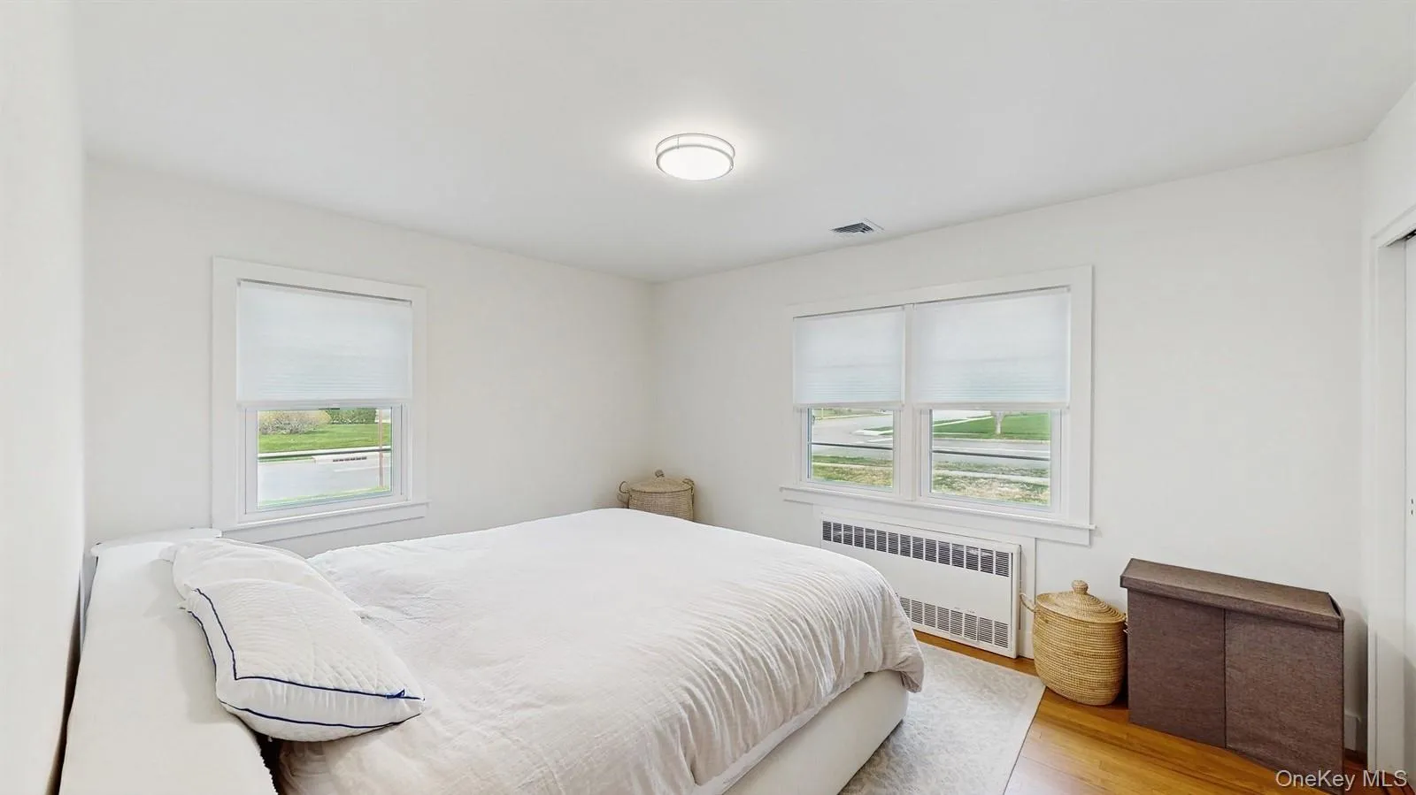 Bedroom featuring visible vents, multiple windows, radiator, and wood finished floors Bedroom featuring visible vents, multiple windows, radiator, and wood finished floors