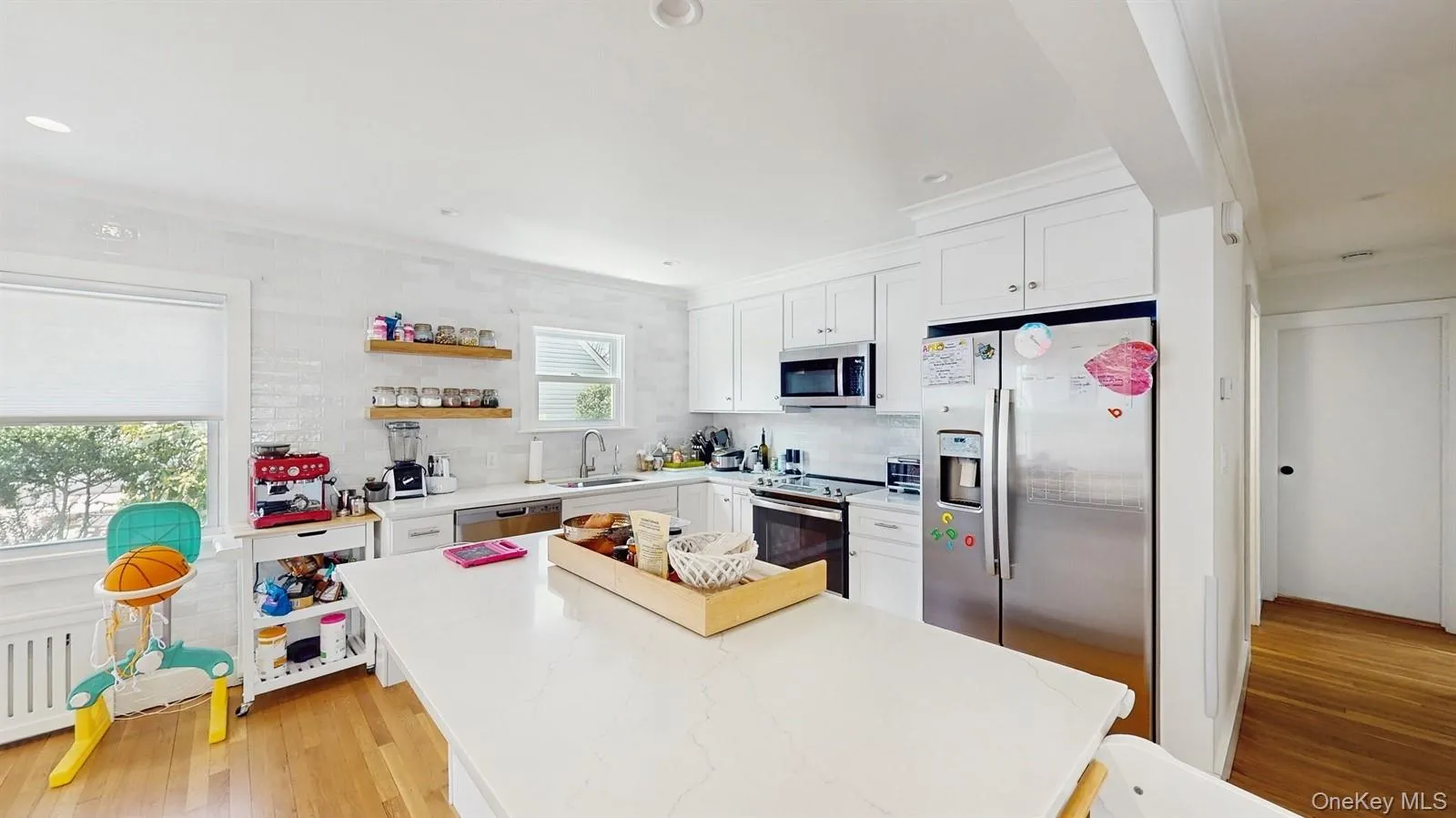 Kitchen featuring light wood-style flooring, white cabinetry, a kitchen island, a sink, and stainless steel appliances Kitchen featuring light wood-style flooring, white cabinetry, a kitchen island, a sink, and stainless steel appliances