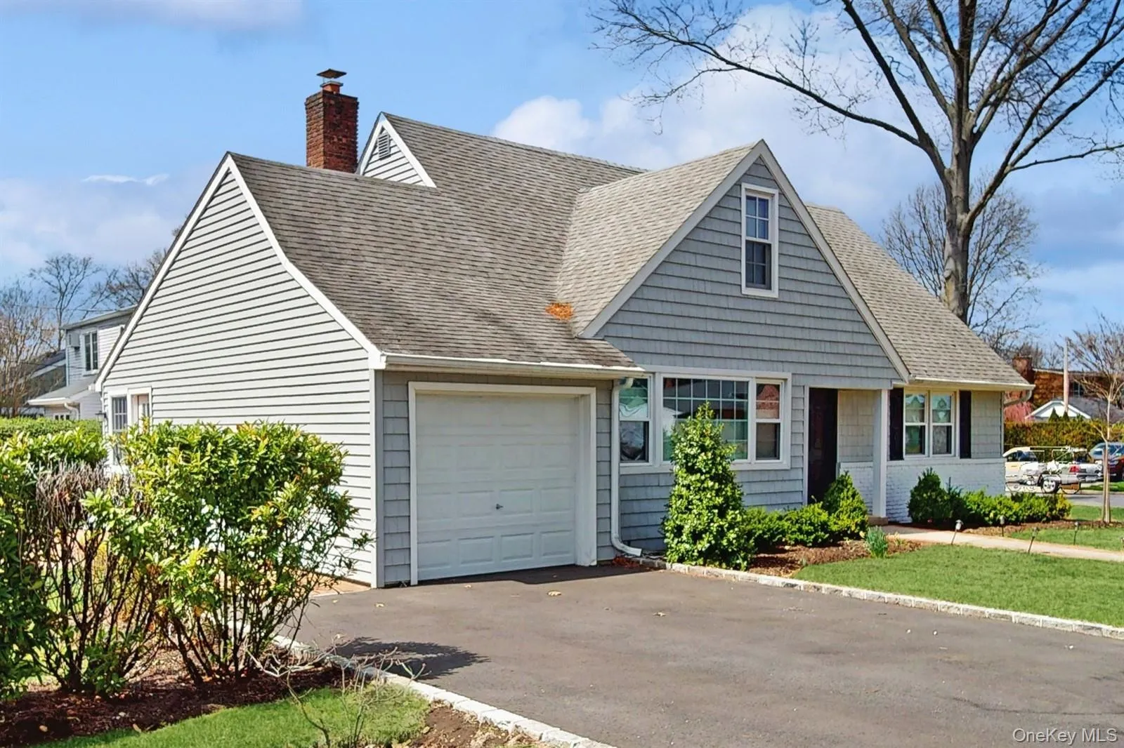 New england style home with a garage, driveway, a chimney, and a shingled roof New england style home with a garage, driveway, a chimney, and a shingled roof