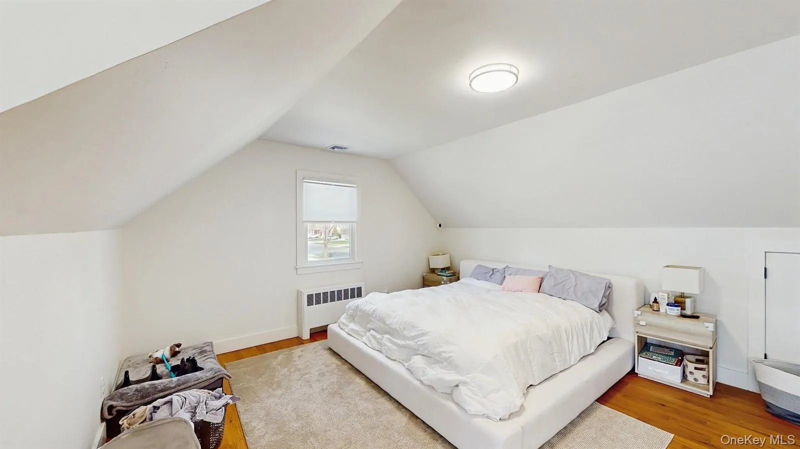 Bedroom with visible vents, radiator heating unit, vaulted ceiling, and wood finished floors Bedroom with visible vents, radiator heating unit, vaulted ceiling, and wood finished floors