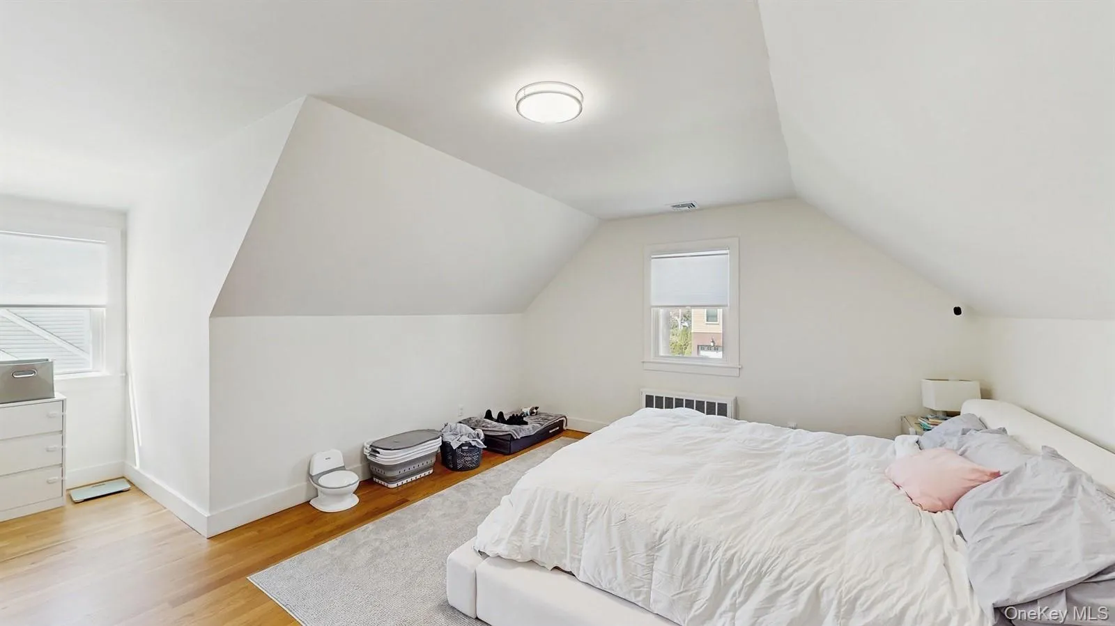 Bedroom featuring visible vents, baseboards, light wood finished floors, radiator, and lofted ceiling Bedroom featuring visible vents, baseboards, light wood finished floors, radiator, and lofted ceiling