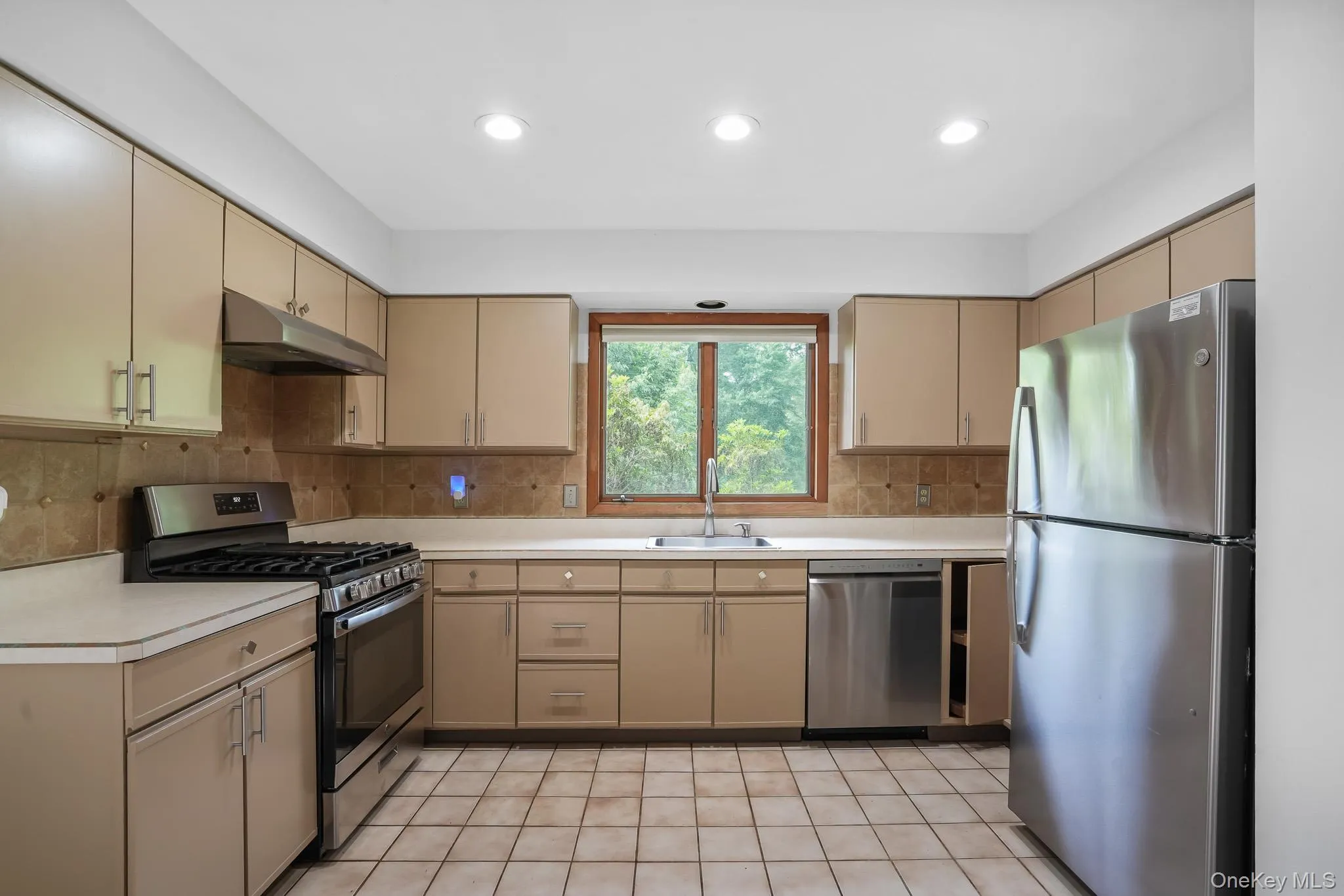 Kitchen featuring neutral cabinetry, stainless steel appliances, tile flooring, and a tile backsplash Kitchen featuring neutral cabinetry, stainless steel appliances, tile flooring, and a tile backsplash