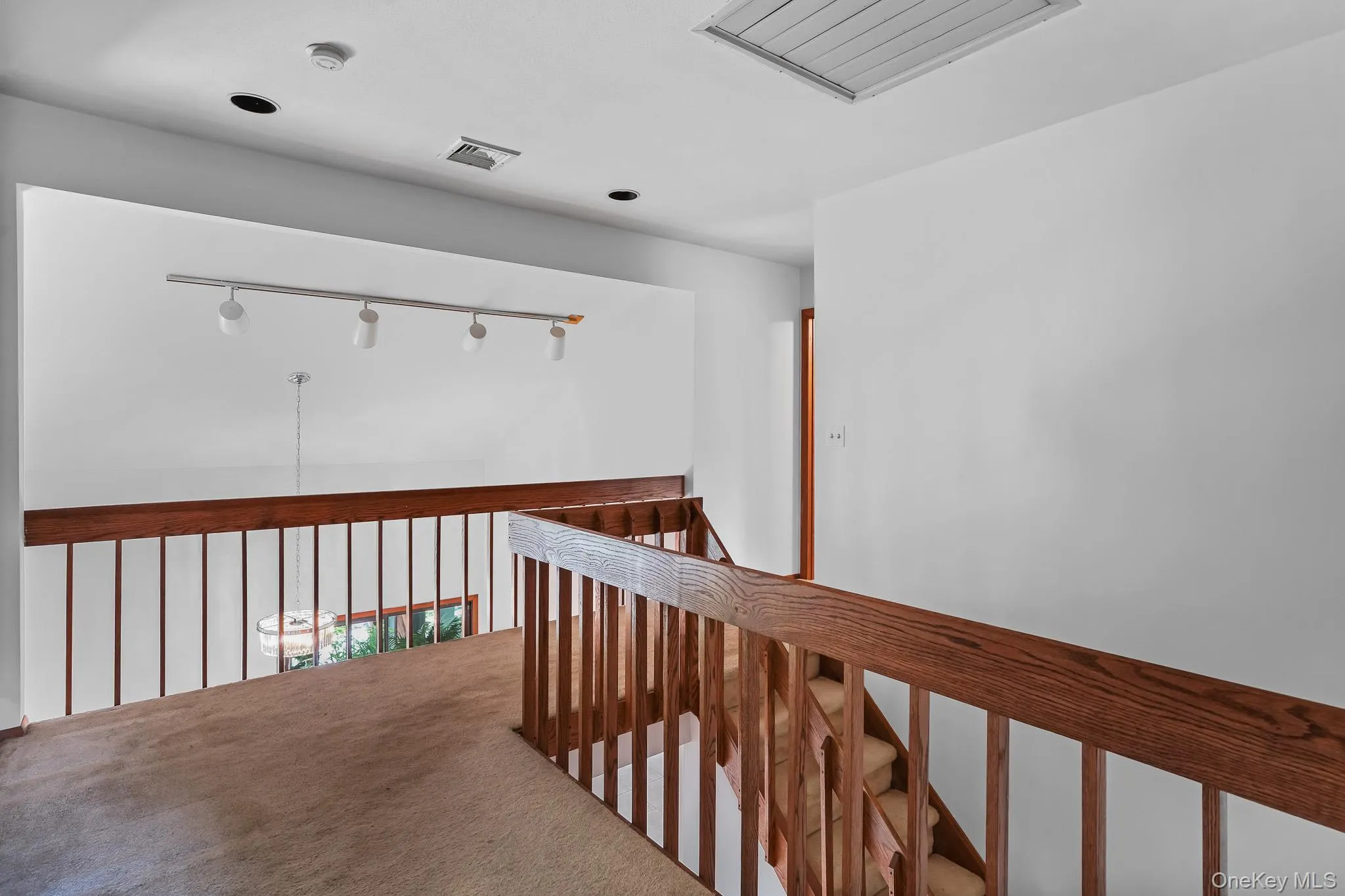 Upper-level landing featuring a wood-finish railing, light beige carpet flooring, recessed ceiling lighting, and a white ceiling with an attic access panel Upper-level landing featuring a wood-finish railing, light beige carpet flooring, recessed ceiling lighting, and a white ceiling with an attic access panel