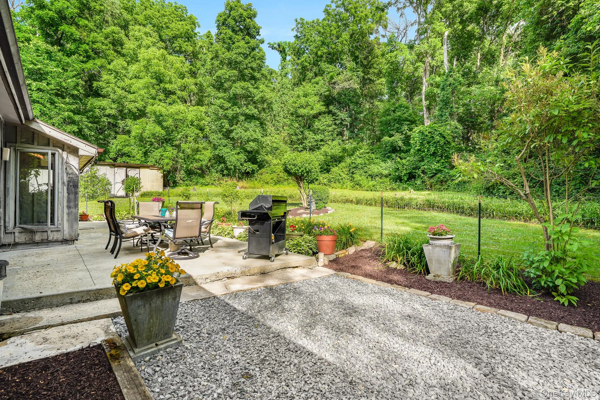 Stone patio with direct outdoor access, featuring a gravel area and manicured lawn surrounded by mature trees Stone patio with direct outdoor access, featuring a gravel area and manicured lawn surrounded by mature trees