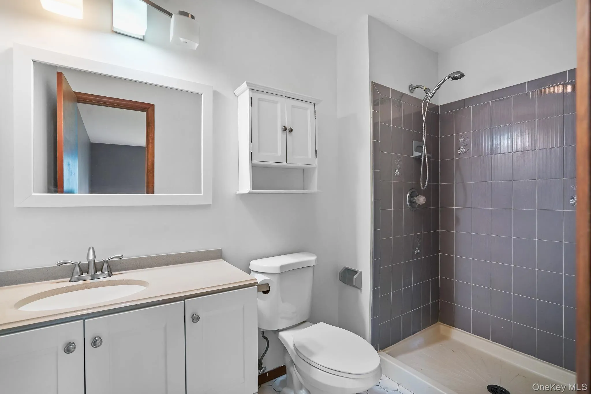 Bathroom featuring a white vanity with a light-toned countertop, a rectangular mirror, and an overhead light fixture Bathroom featuring a white vanity with a light-toned countertop, a rectangular mirror, and an overhead light fixture