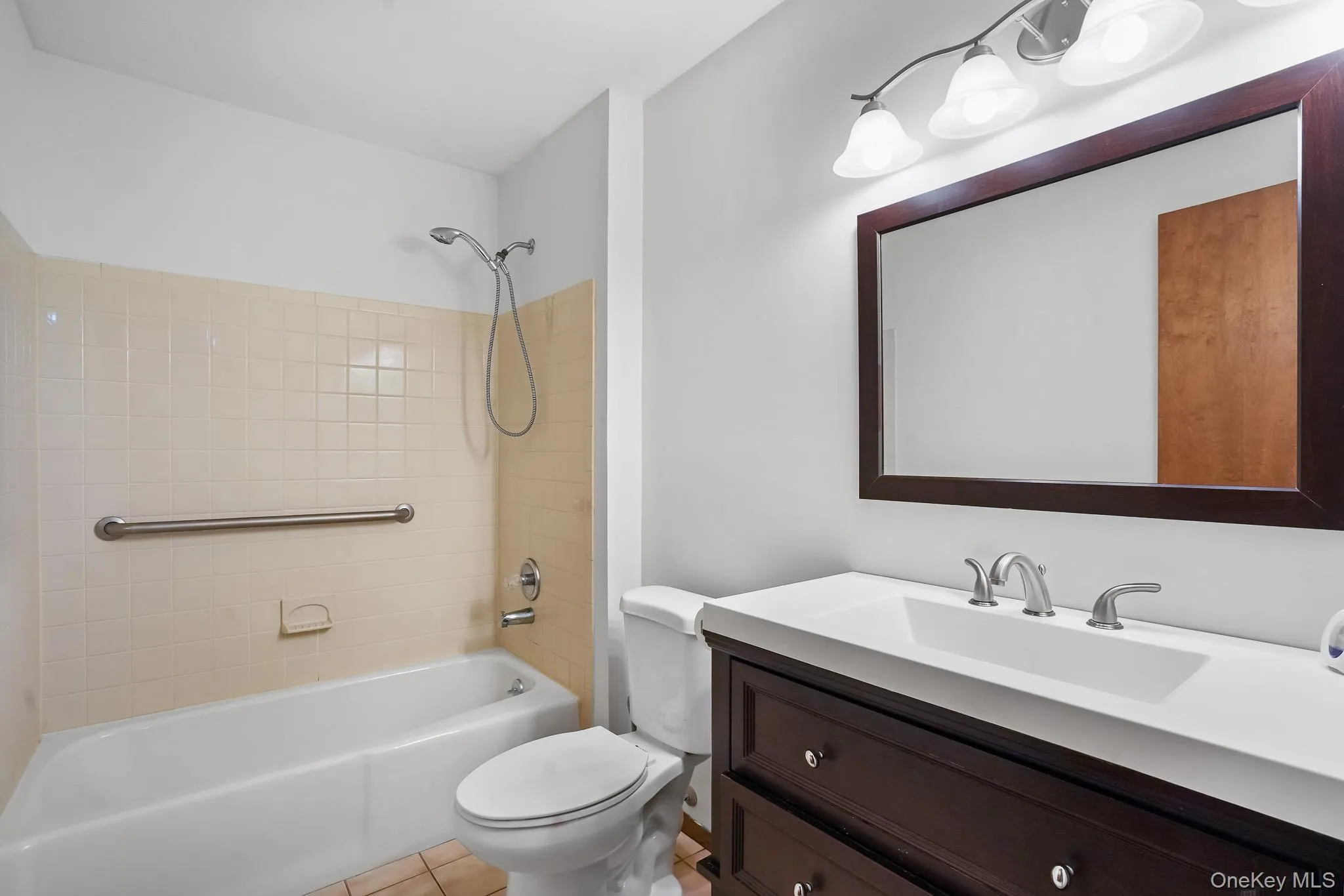 Bathroom featuring a dark wood-finish vanity with a white integrated sink, a large framed mirror, and a three-light vanity fixture Bathroom featuring a dark wood-finish vanity with a white integrated sink, a large framed mirror, and a three-light vanity fixture