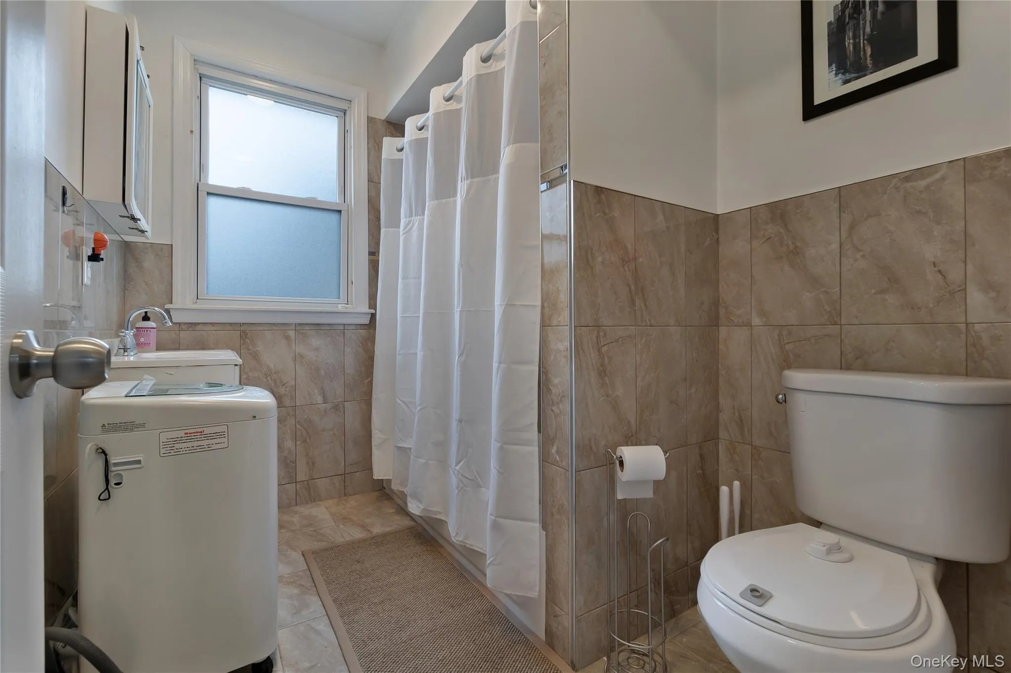 Bathroom featuring floor-to-ceiling tile, a single-pane window, and a built-in toilet Bathroom featuring floor-to-ceiling tile, a single-pane window, and a built-in toilet