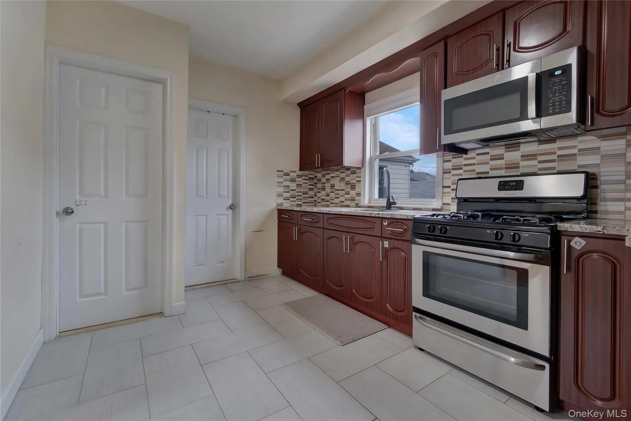 Kitchen featuring stainless steel appliances, rich wood-finish cabinetry, granite countertops, and a mosaic tile backsplash Kitchen featuring stainless steel appliances, rich wood-finish cabinetry, granite countertops, and a mosaic tile backsplash