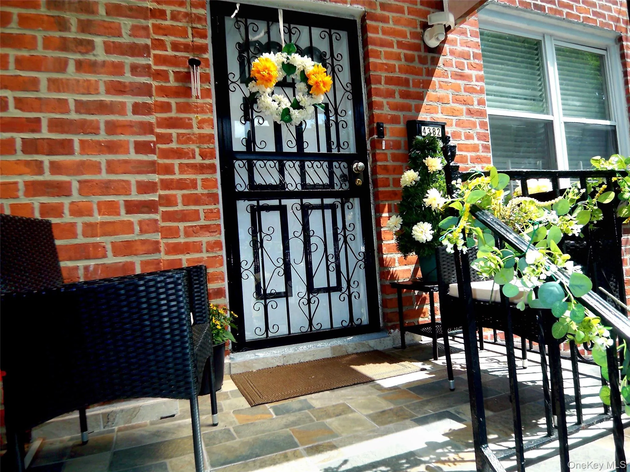 Brick facade entry featuring a black security door with scrollwork, multi-tone slate tile flooring, and a black wrought iron railing Brick facade entry featuring a black security door with scrollwork, multi-tone slate tile flooring, and a black wrought iron railing