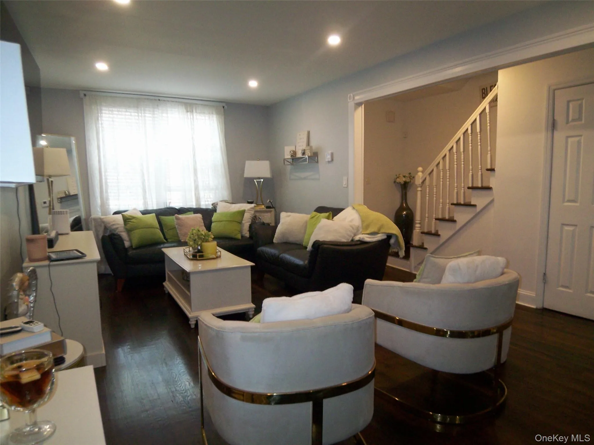 Spacious living area featuring dark wood-finish flooring, recessed lighting, and a window with blinds and sheer curtains Spacious living area featuring dark wood-finish flooring, recessed lighting, and a window with blinds and sheer curtains