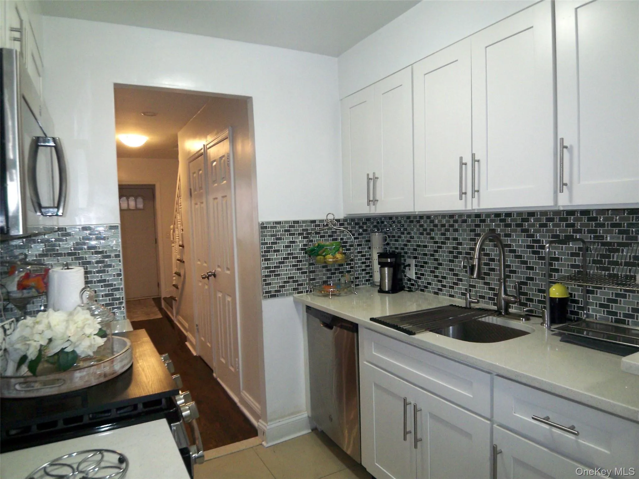 Kitchen featuring white shaker-style cabinetry, mosaic tile backsplash, stainless steel appliances, a double basin sink with a high-arc faucet, and light-toned countertops Kitchen featuring white shaker-style cabinetry, mosaic tile backsplash, stainless steel appliances, a double basin sink with a high-arc faucet, and light-toned countertops
