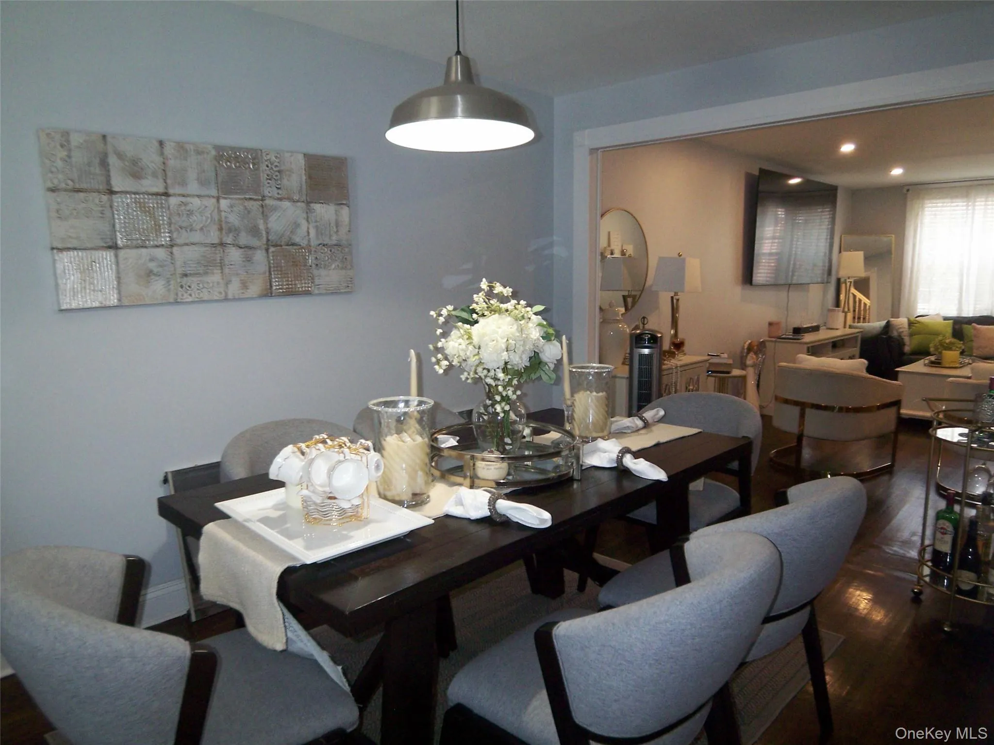 Dining area featuring dark wood-finish flooring, a contemporary pendant light fixture, and an open doorway to an adjacent living space Dining area featuring dark wood-finish flooring, a contemporary pendant light fixture, and an open doorway to an adjacent living space