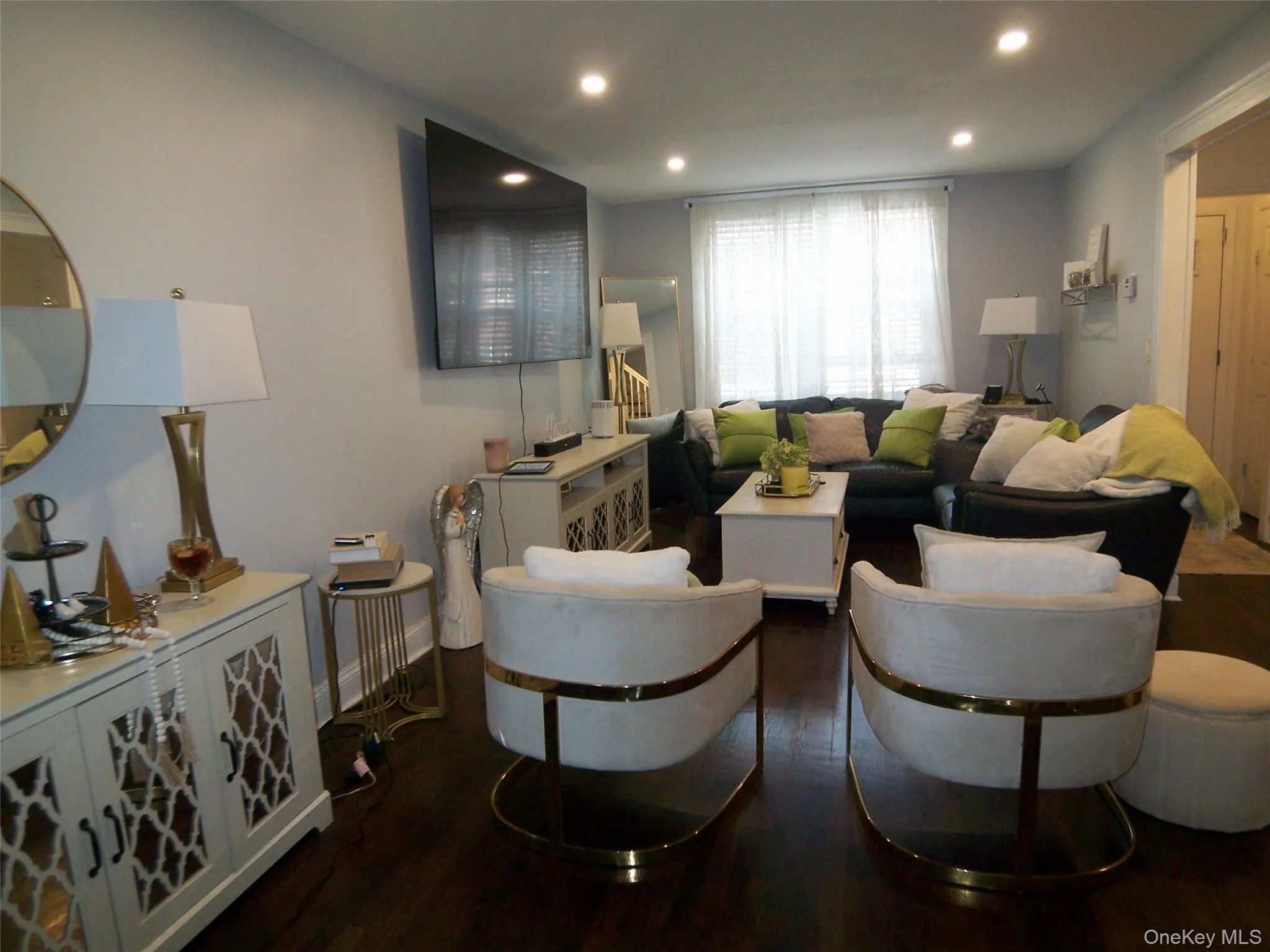 Spacious living area featuring dark wood-finish flooring, recessed lighting, and a large window with privacy blinds Spacious living area featuring dark wood-finish flooring, recessed lighting, and a large window with privacy blinds