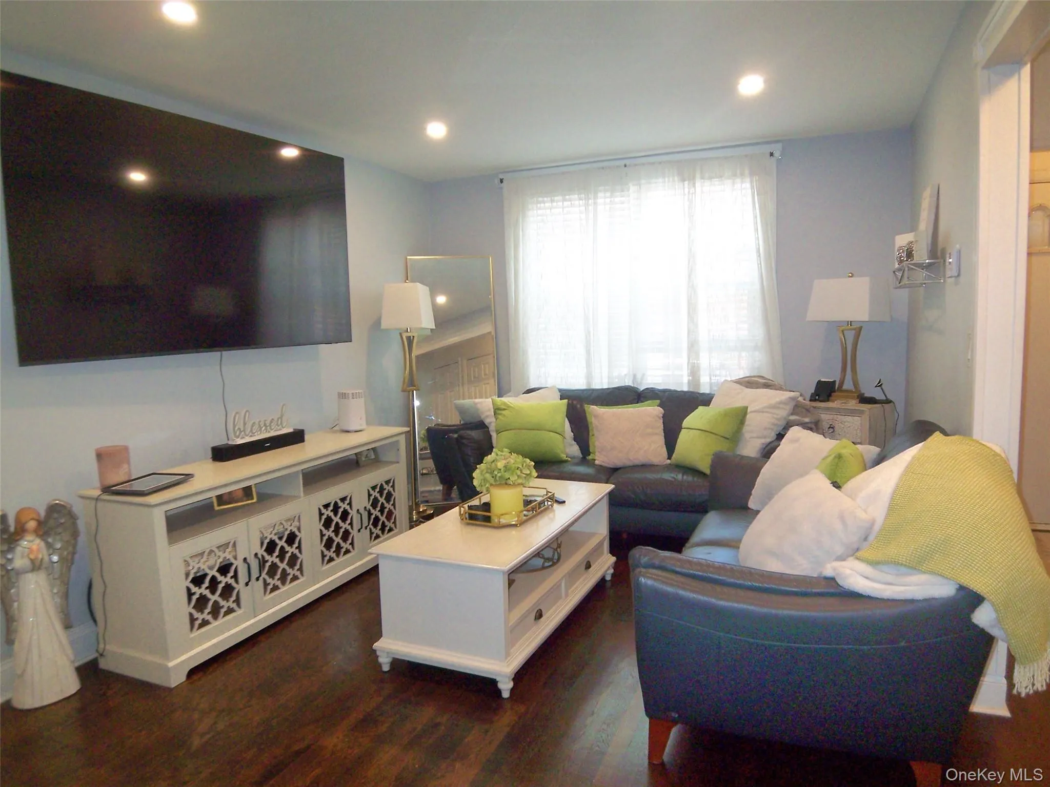 Living area featuring recessed lighting, a large window with sheers, wood-finish flooring, and light blue walls Living area featuring recessed lighting, a large window with sheers, wood-finish flooring, and light blue walls