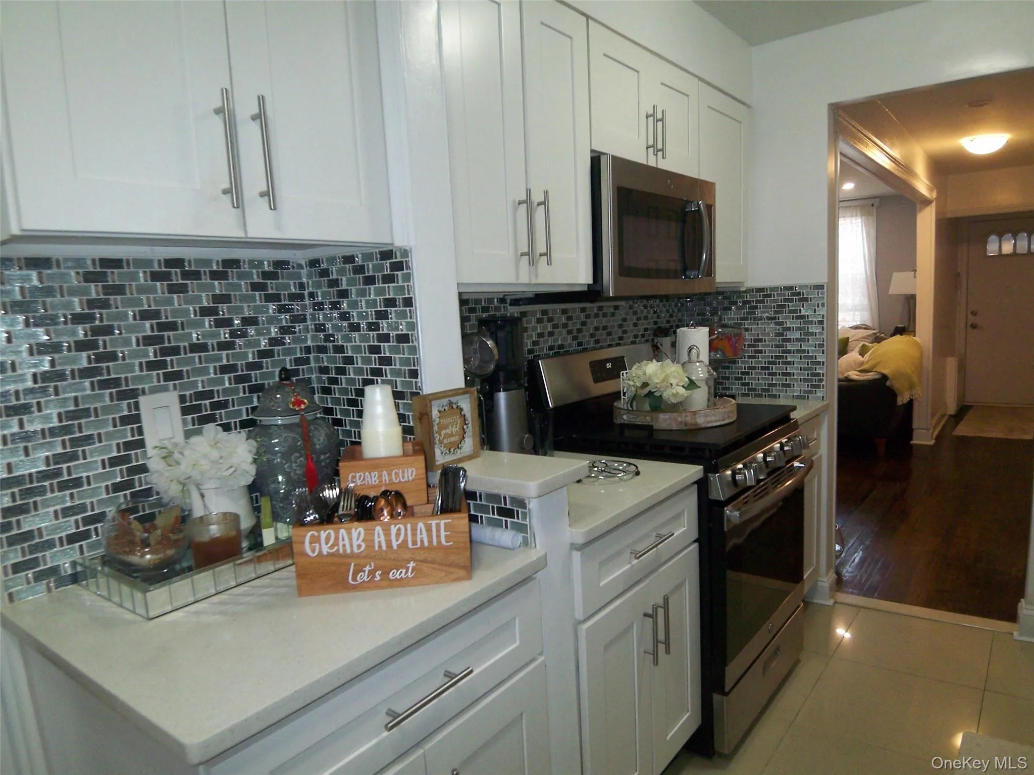 Modern kitchen featuring white cabinetry with brushed nickel hardware, light-toned countertops, and a full tile backsplash Modern kitchen featuring white cabinetry with brushed nickel hardware, light-toned countertops, and a full tile backsplash