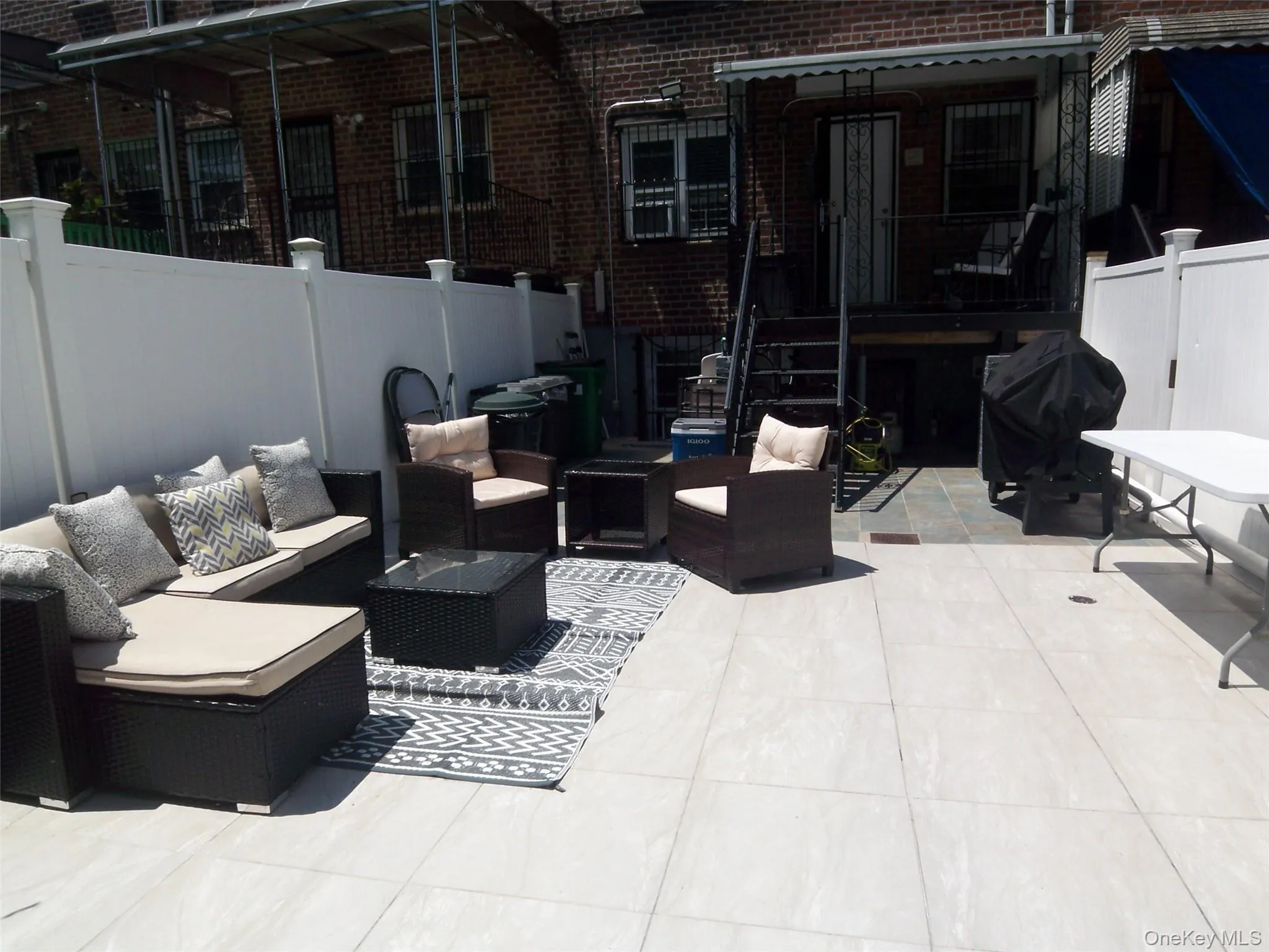 Spacious patio featuring light-toned tile flooring, white vinyl fencing, and a brick exterior with a protective awning Spacious patio featuring light-toned tile flooring, white vinyl fencing, and a brick exterior with a protective awning