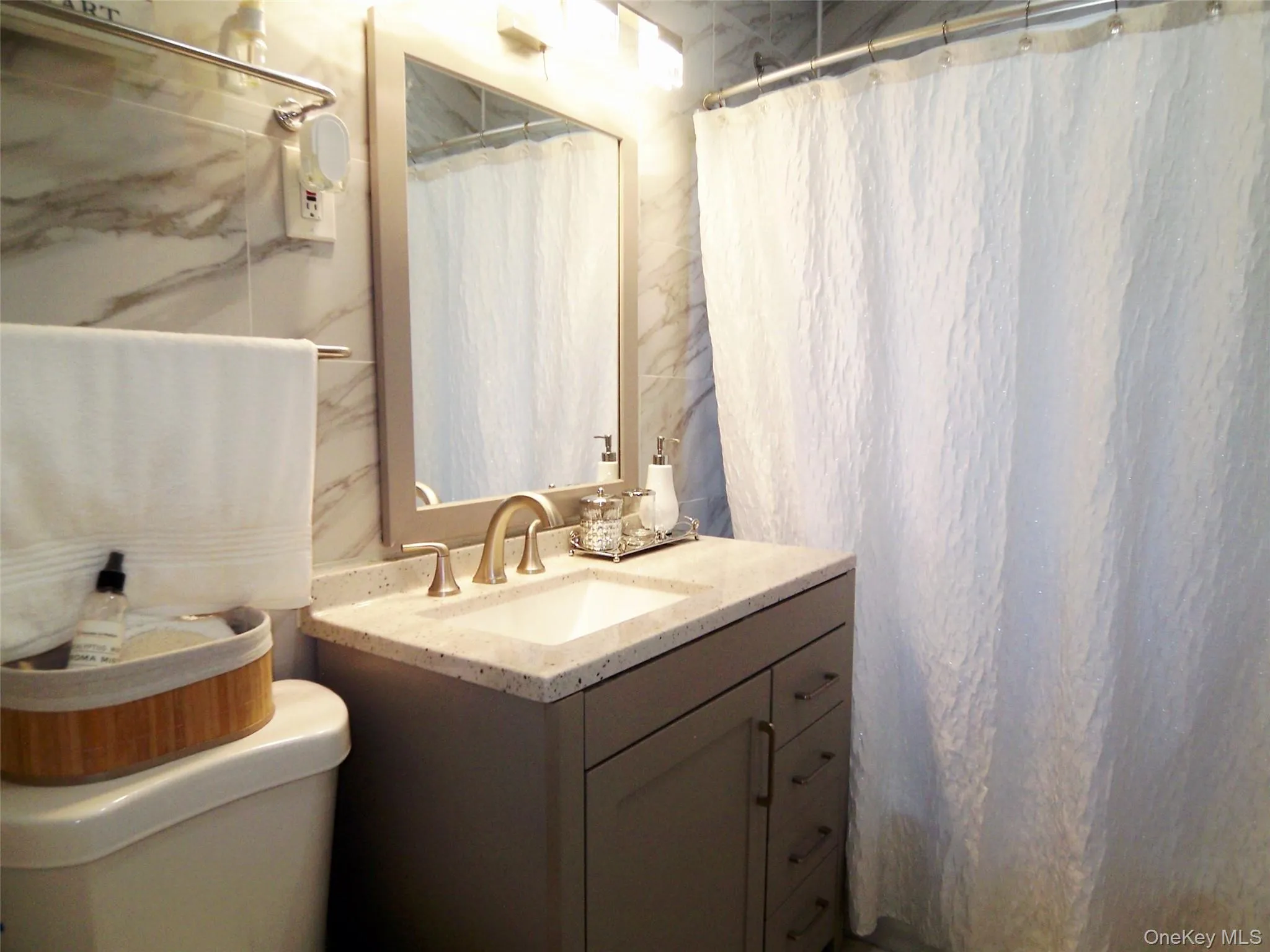 Bathroom featuring a single vanity with a light-colored countertop and integrated sink, framed mirror, and warm metallic faucet Bathroom featuring a single vanity with a light-colored countertop and integrated sink, framed mirror, and warm metallic faucet