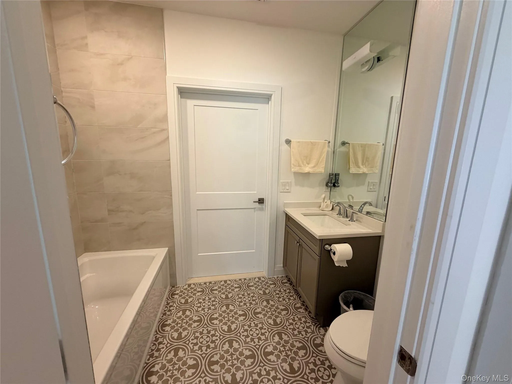 Bathroom with patterned floor tiles, a built-in soaker bathtub, and a vanity featuring a solid surface countertop Bathroom with patterned floor tiles, a built-in soaker bathtub, and a vanity featuring a solid surface countertop