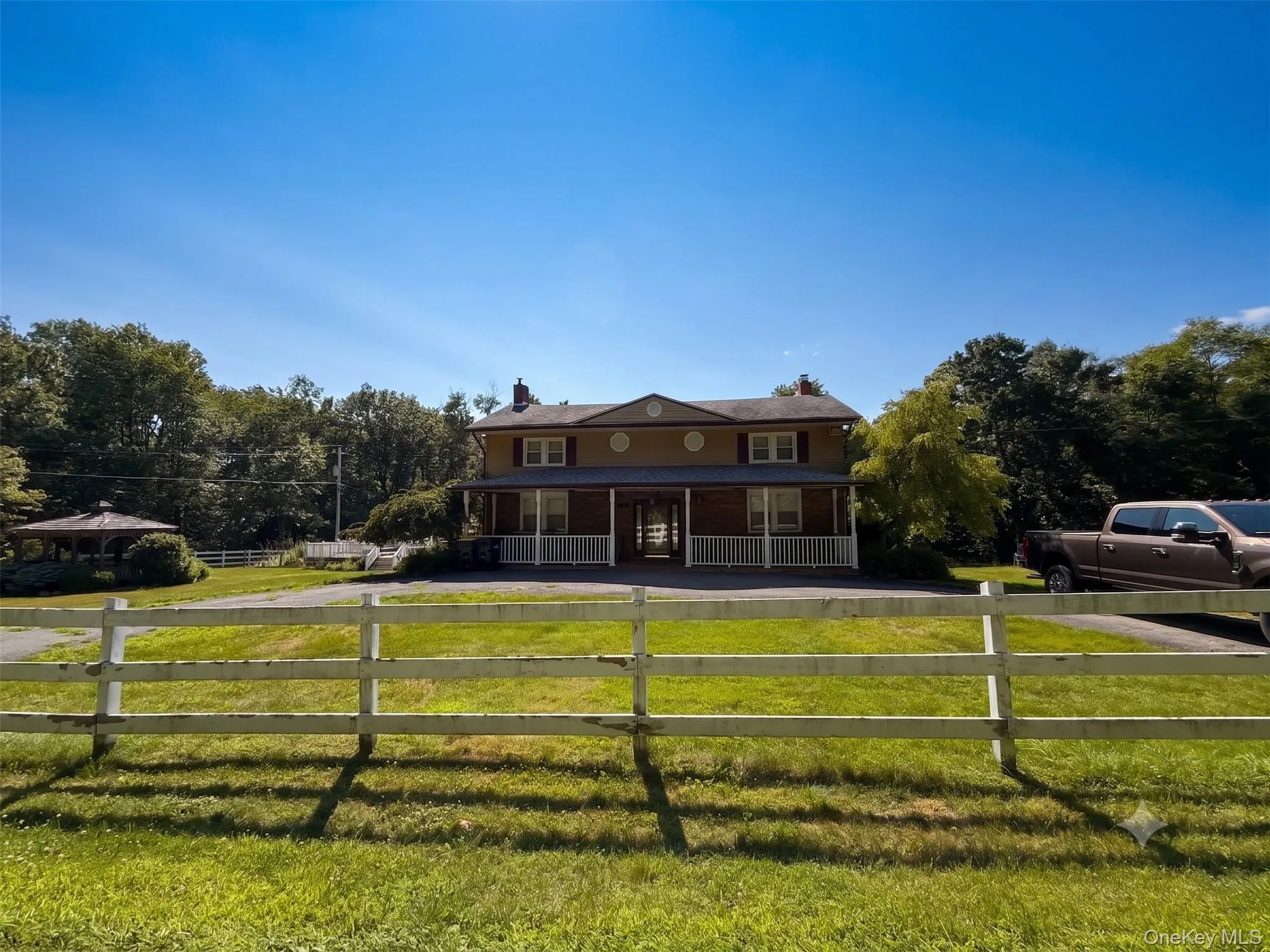 Two-story property featuring a covered porch with white railings, a circular drive, and a detached gazebo Two-story property featuring a covered porch with white railings, a circular drive, and a detached gazebo