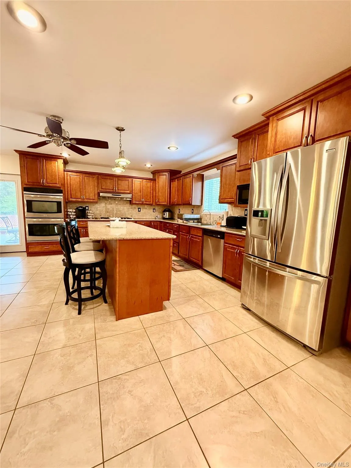 Kitchen featuring a central island with countertop seating, extensive wood cabinetry, stainless steel appliances, and large format tile flooring Kitchen featuring a central island with countertop seating, extensive wood cabinetry, stainless steel appliances, and large format tile flooring