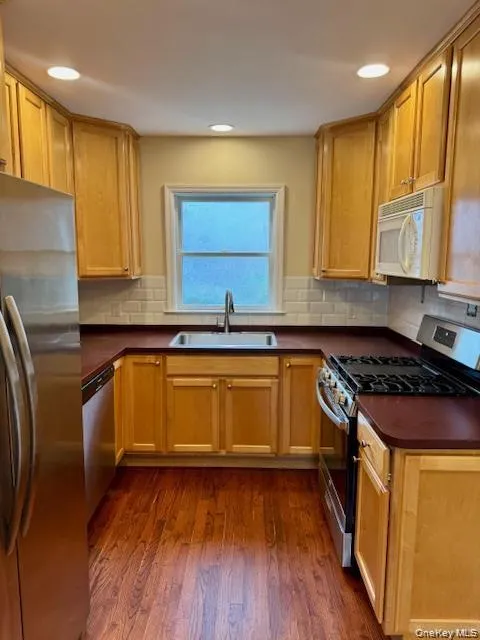 U-shaped kitchen featuring wood-finish cabinetry, dark countertops, and stainless steel appliances U-shaped kitchen featuring wood-finish cabinetry, dark countertops, and stainless steel appliances