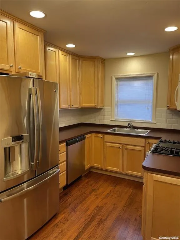 Kitchen featuring wood-finish flooring, recessed lighting, wood cabinetry, stainless steel appliances, and a tile backsplash Kitchen featuring wood-finish flooring, recessed lighting, wood cabinetry, stainless steel appliances, and a tile backsplash