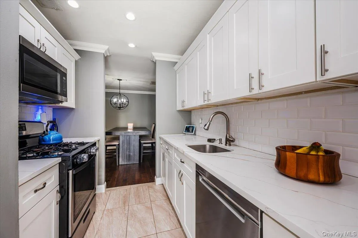 Kitchen featuring a sink, crown molding, stainless steel appliances, and white cabinetry Kitchen featuring a sink, crown molding, stainless steel appliances, and white cabinetry
