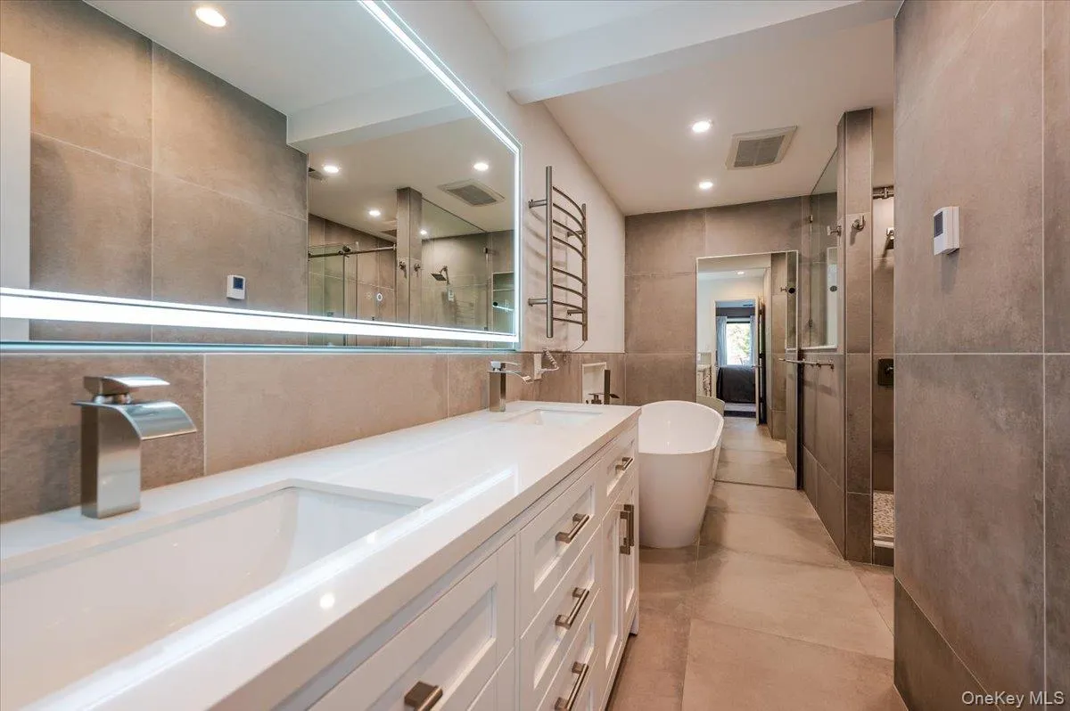 Beautiful primary bath with stand alone tub. Floor to ceiling tile, double vanity with lighted mirror. Glass enclosed tiled shower and heated towel bar. Beautiful primary bath with stand alone tub. Floor to ceiling tile, double vanity with lighted mirror. Glass enclosed tiled shower and heated towel bar.