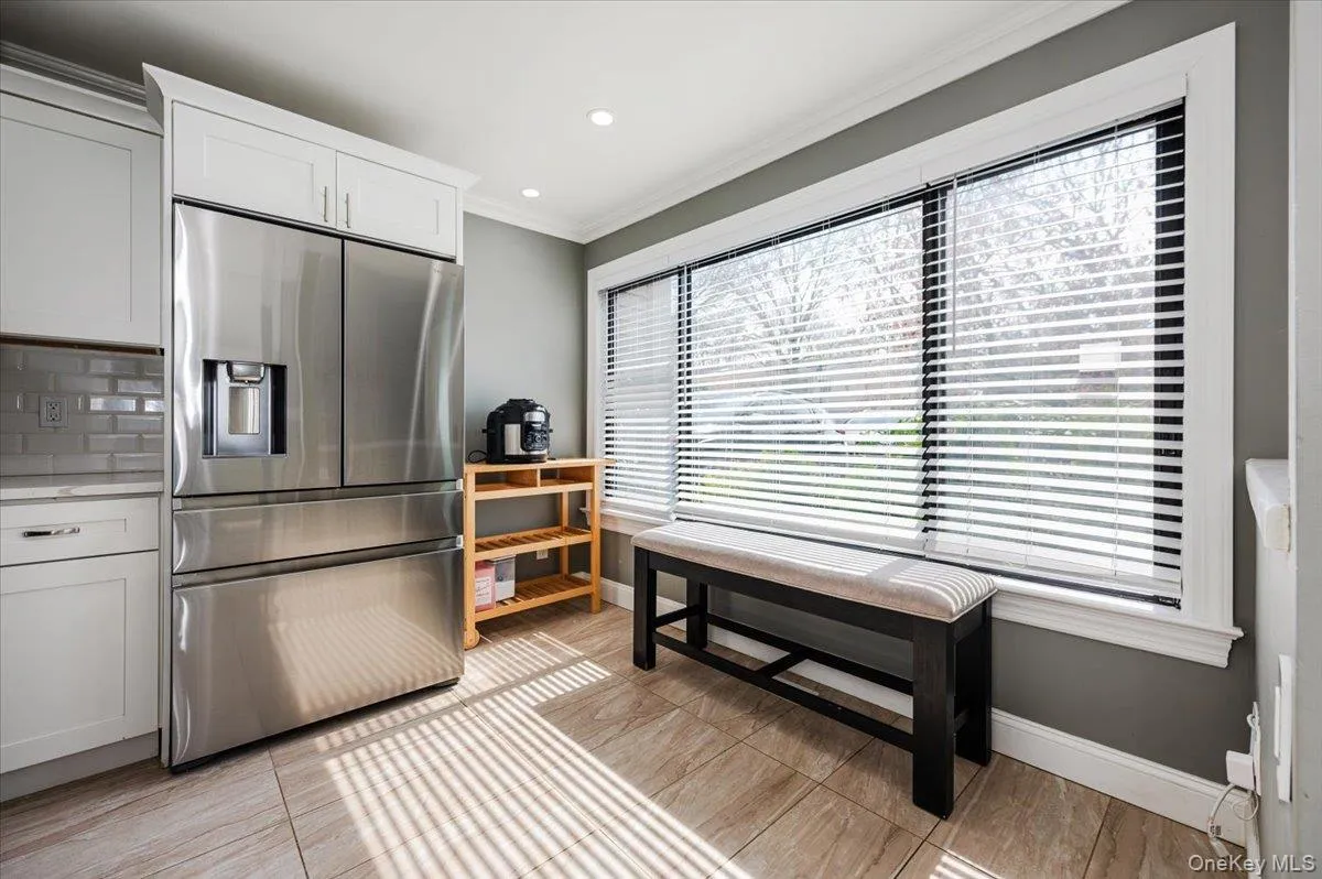Kitchen with crown molding, light countertops, baseboards, white cabinets, and stainless steel fridge Kitchen with crown molding, light countertops, baseboards, white cabinets, and stainless steel fridge