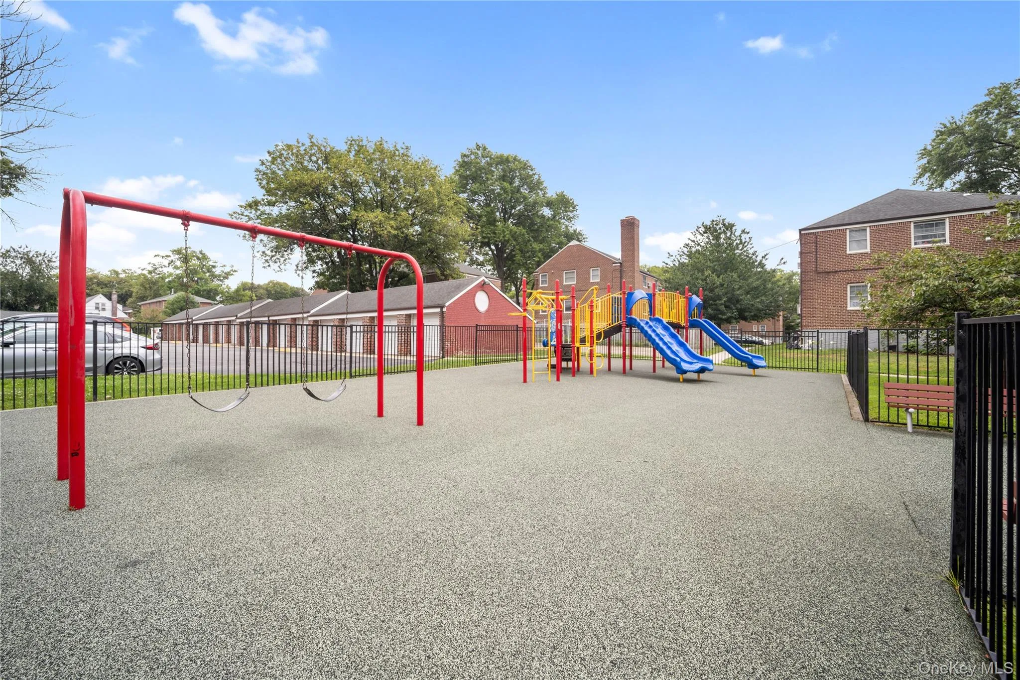 Outdoor playground featuring a red swing set, colorful slide structure, and a fenced perimeter Outdoor playground featuring a red swing set, colorful slide structure, and a fenced perimeter
