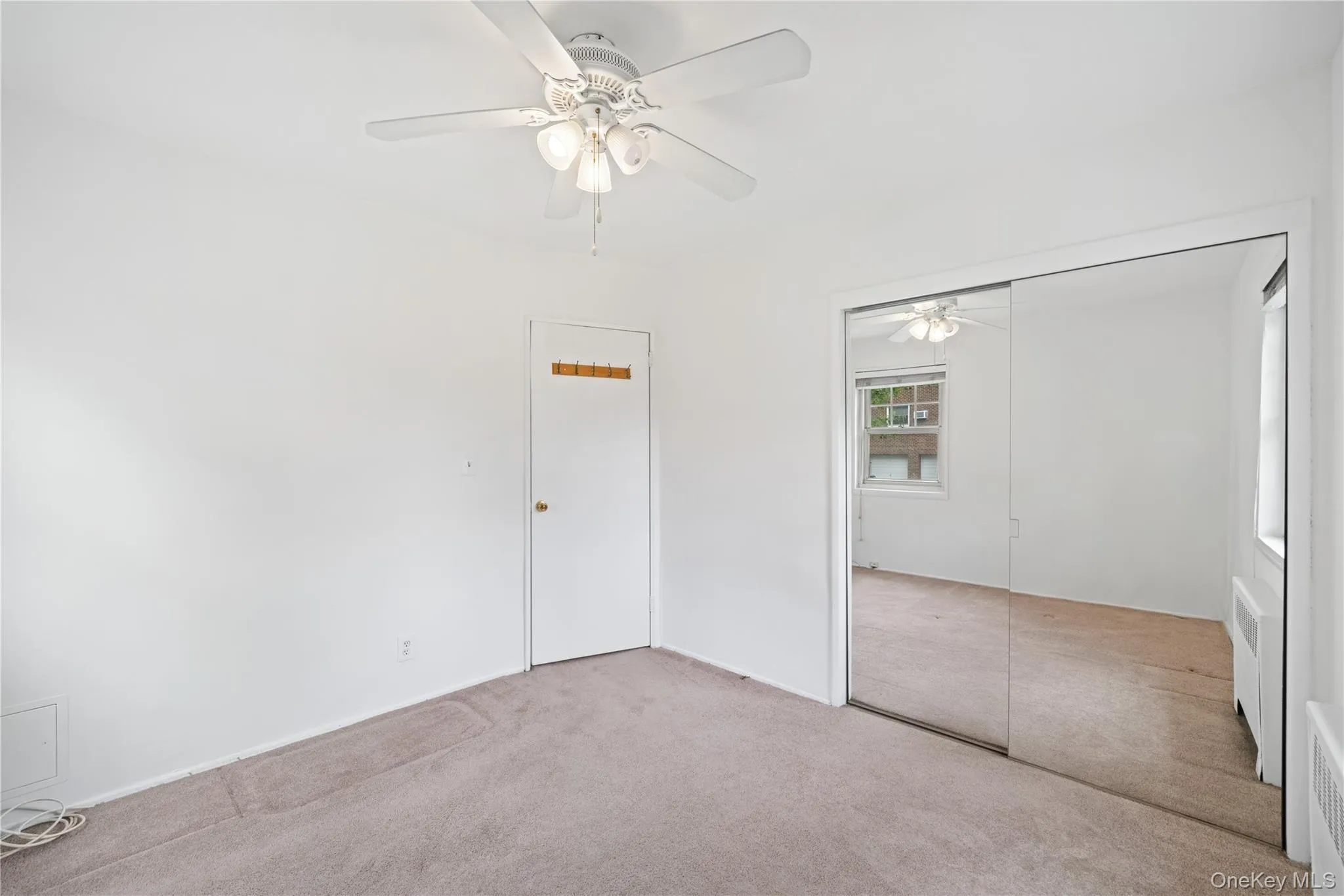 Carpeted room featuring a ceiling fan with integrated lighting, mirrored sliding closet doors, and white walls Carpeted room featuring a ceiling fan with integrated lighting, mirrored sliding closet doors, and white walls