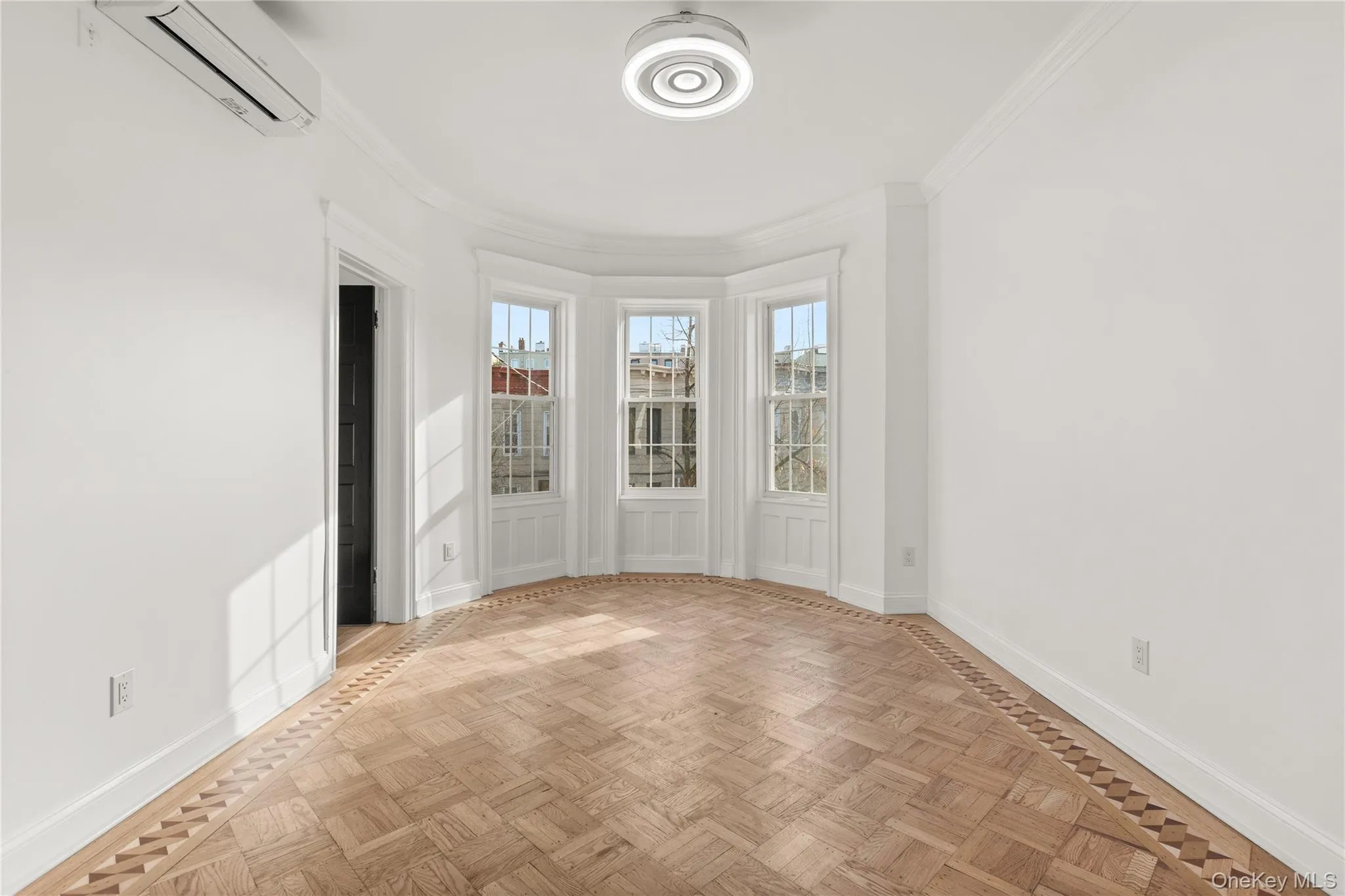 Bedroom with bay window with three individual sash windows, parquet wood flooring with perimeter inlay, crown molding, and a ceiling-mounted light fixture Bedroom with bay window with three individual sash windows, parquet wood flooring with perimeter inlay, crown molding, and a ceiling-mounted light fixture