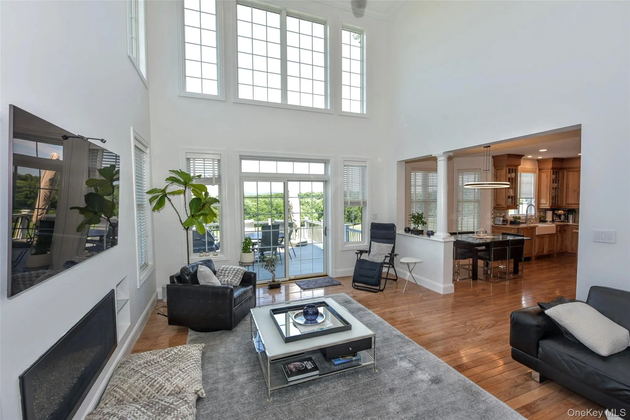 Vaulted living area with wood-finish flooring, featuring a linear fireplace, multiple large windows, and sliding glass doors opening to an outdoor deck Vaulted living area with wood-finish flooring, featuring a linear fireplace, multiple large windows, and sliding glass doors opening to an outdoor deck