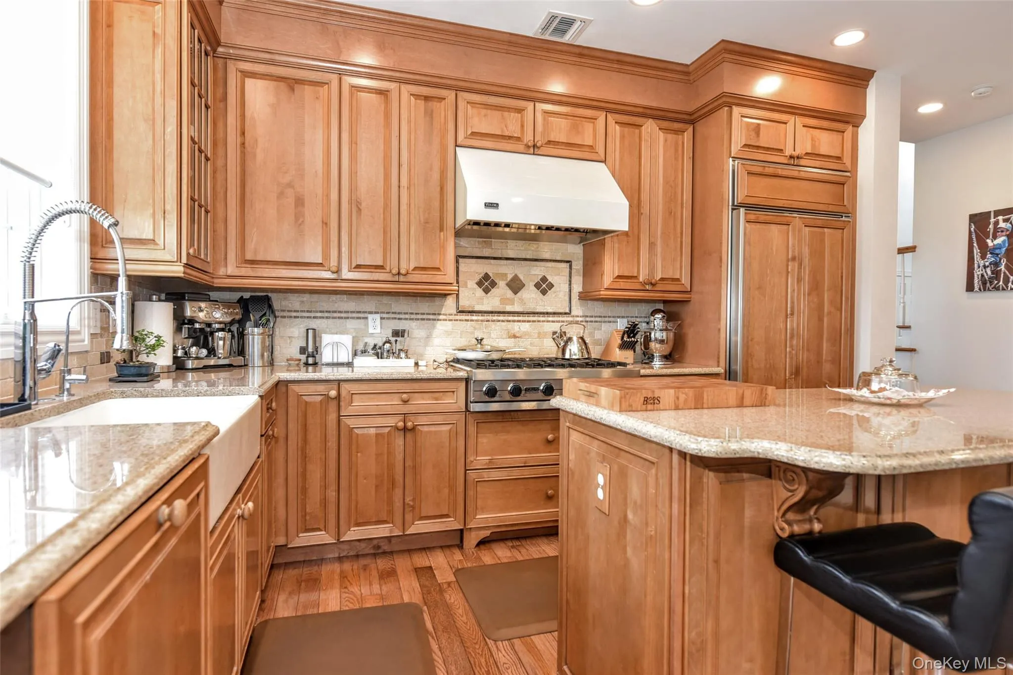 Kitchen featuring wood-finish cabinetry, granite countertops, an undermount farmhouse sink, stainless steel appliances, and wood-finish flooring Kitchen featuring wood-finish cabinetry, granite countertops, an undermount farmhouse sink, stainless steel appliances, and wood-finish flooring