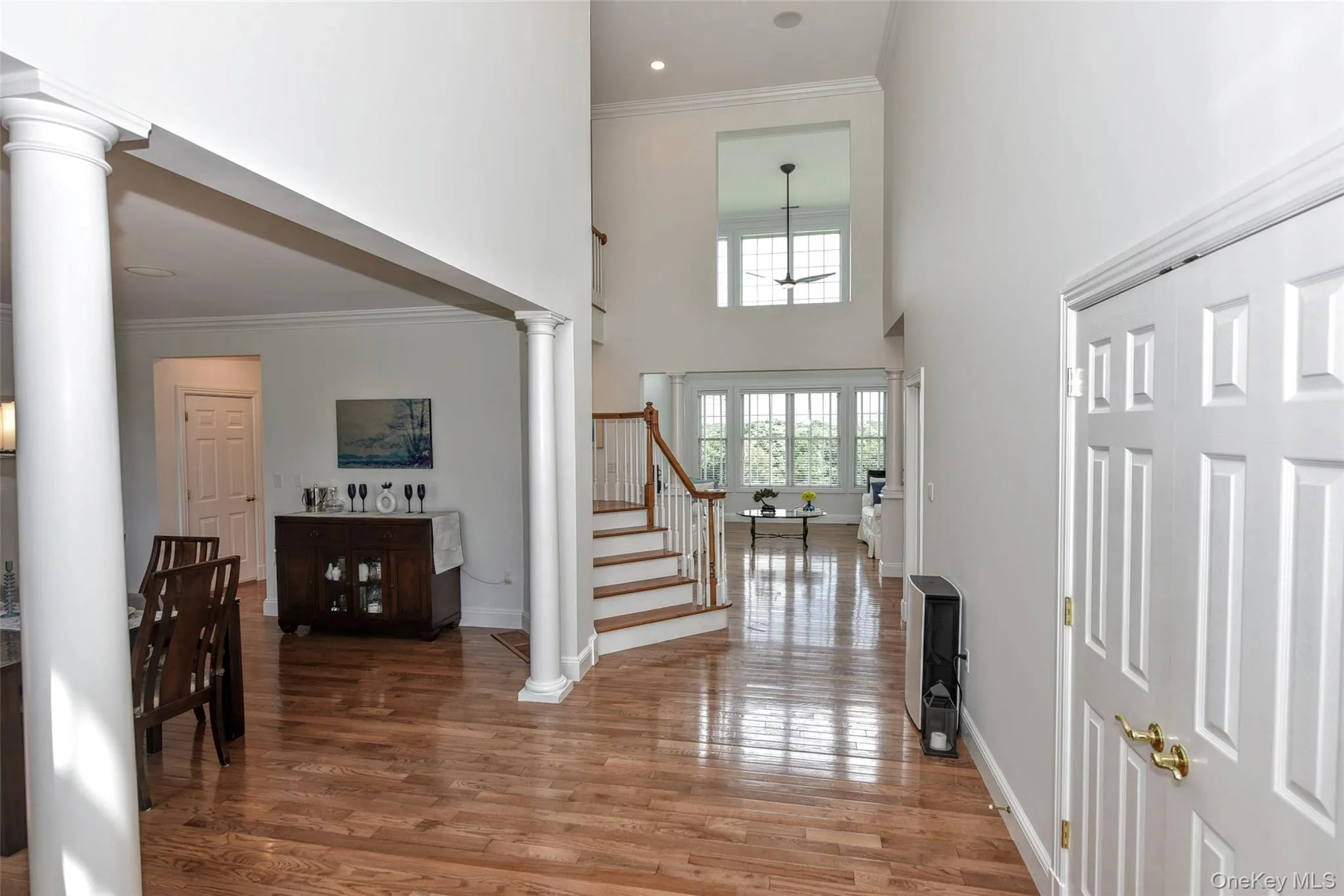 Two-story foyer featuring wood-finish flooring, a grand staircase with white risers and wood treads, and architectural columns Two-story foyer featuring wood-finish flooring, a grand staircase with white risers and wood treads, and architectural columns