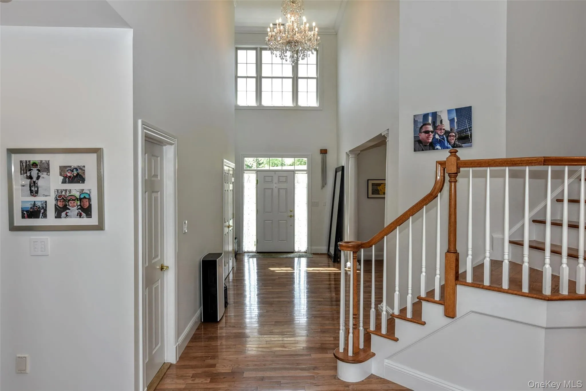 Two-story foyer featuring wood-finish flooring, a grand staircase with wood newel posts and handrail Two-story foyer featuring wood-finish flooring, a grand staircase with wood newel posts and handrail