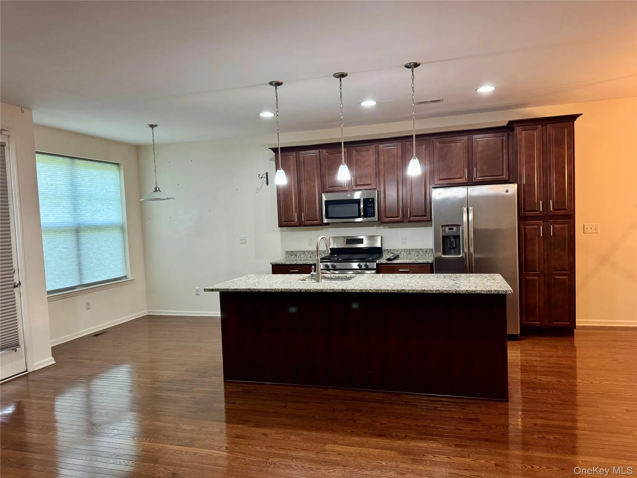 Kitchen with appliances with stainless steel finishes, dark wood finished floors, a kitchen island with sink, dark brown cabinets, and decorative light fixtures Kitchen with appliances with stainless steel finishes, dark wood finished floors, a kitchen island with sink, dark brown cabinets, and decorative light fixtures